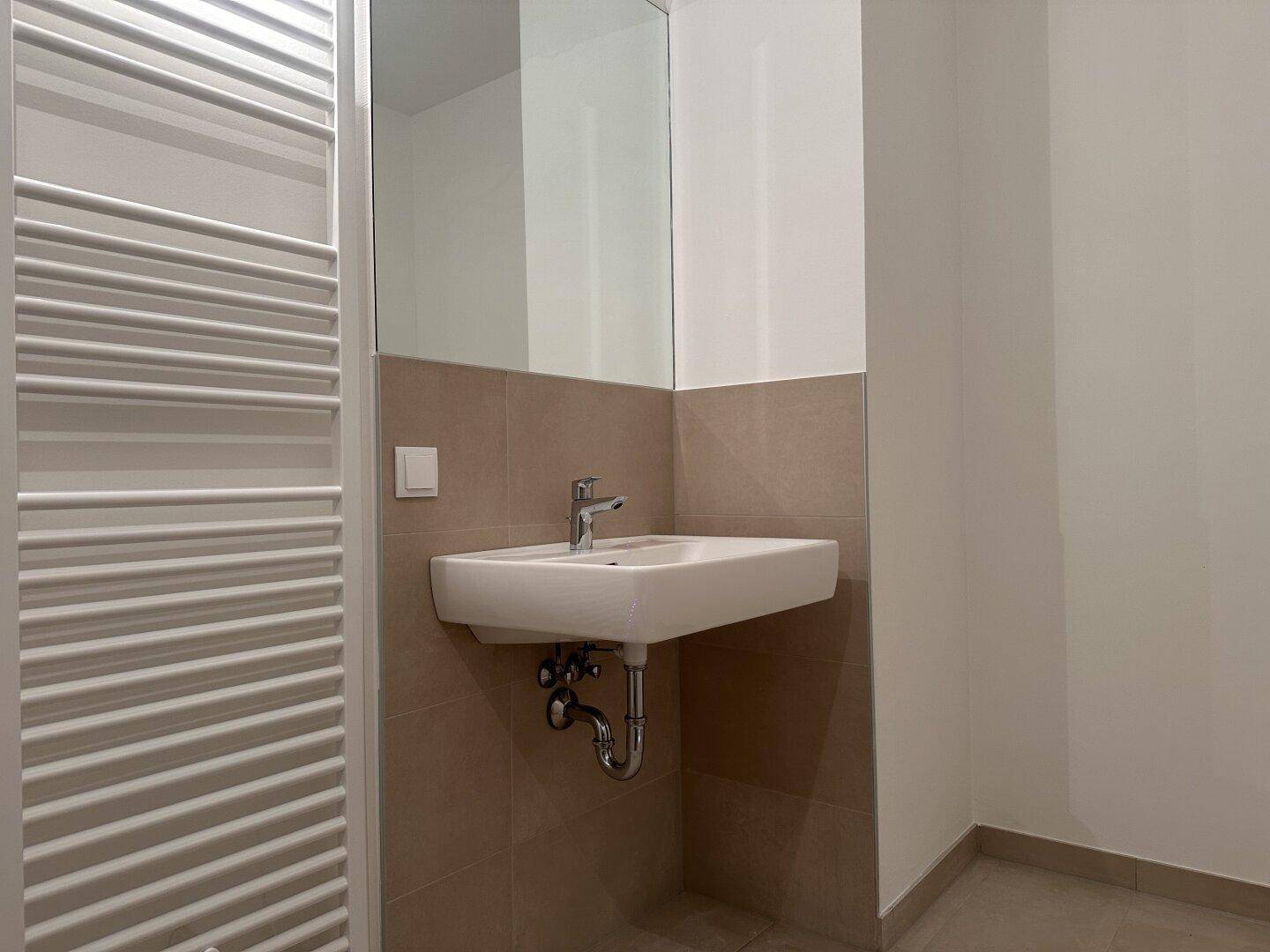 Badezimmer mit Waschbecken, großem Spiegel und beheiztem Handtuchhalter.