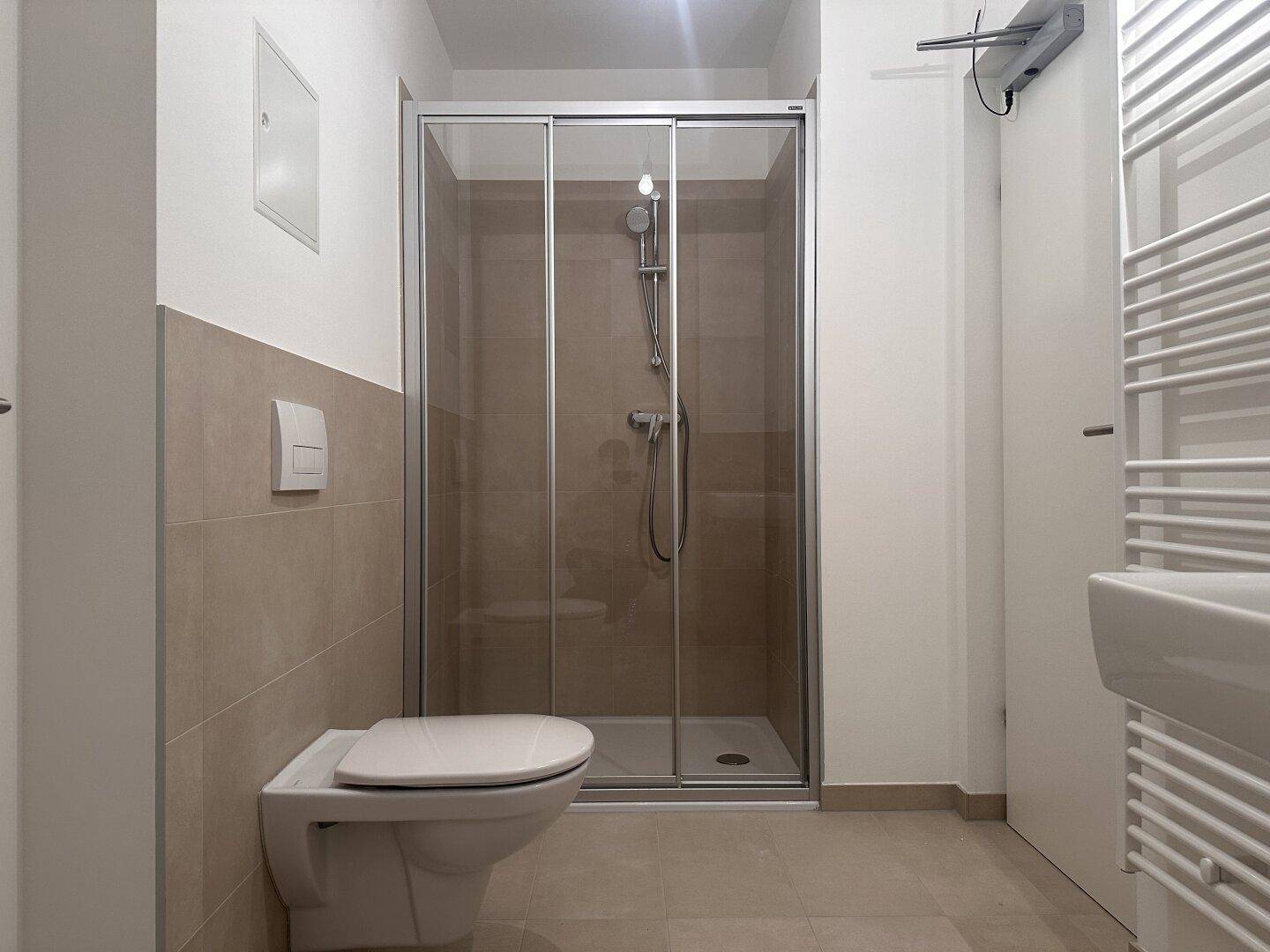 Modernes Badezimmer mit wandhängendem WC und Duschkabine mit Glasschiebetür.