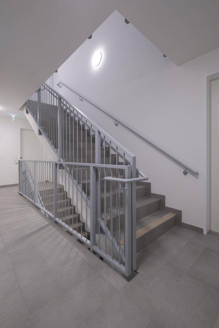 Modernes Treppenhaus mit Metallgeländer und Fliesenboden in einem Mehrfamilienhaus.
