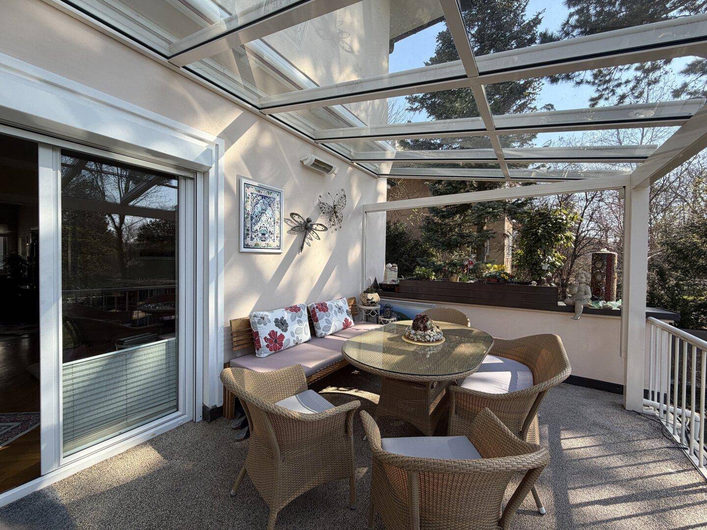 Überdachte Terrasse mit Glasdach und bequemen Gartenmöbeln, ideal für entspannte Stunden.