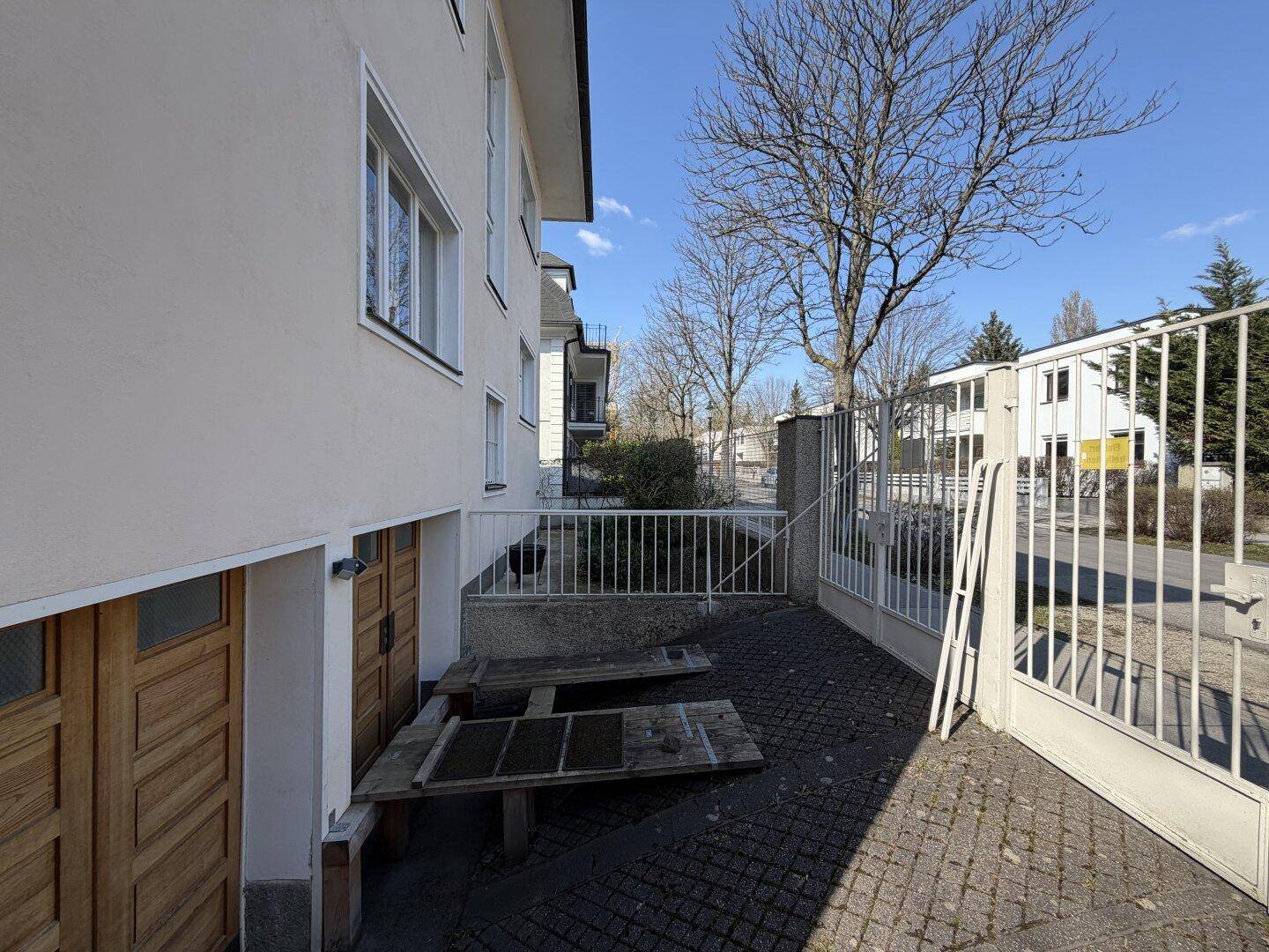 Seitenansicht des Hauses mit Garagentoren und gepflastertem Bereich, umgeben von einem Zaun.