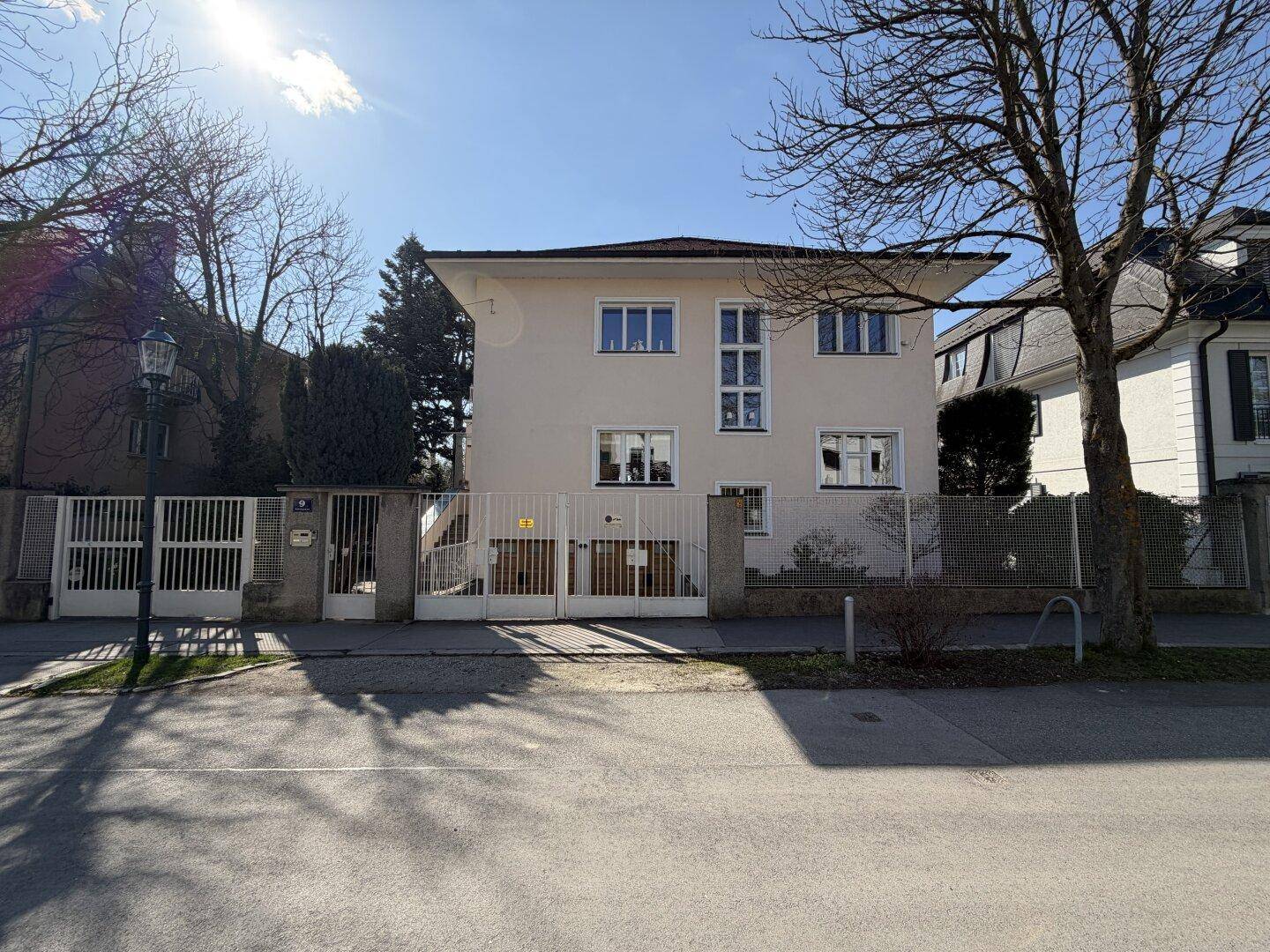 Frontansicht des Hauses von der Straße mit Eingangstor und klassischer Architektur unter blauem Himmel.