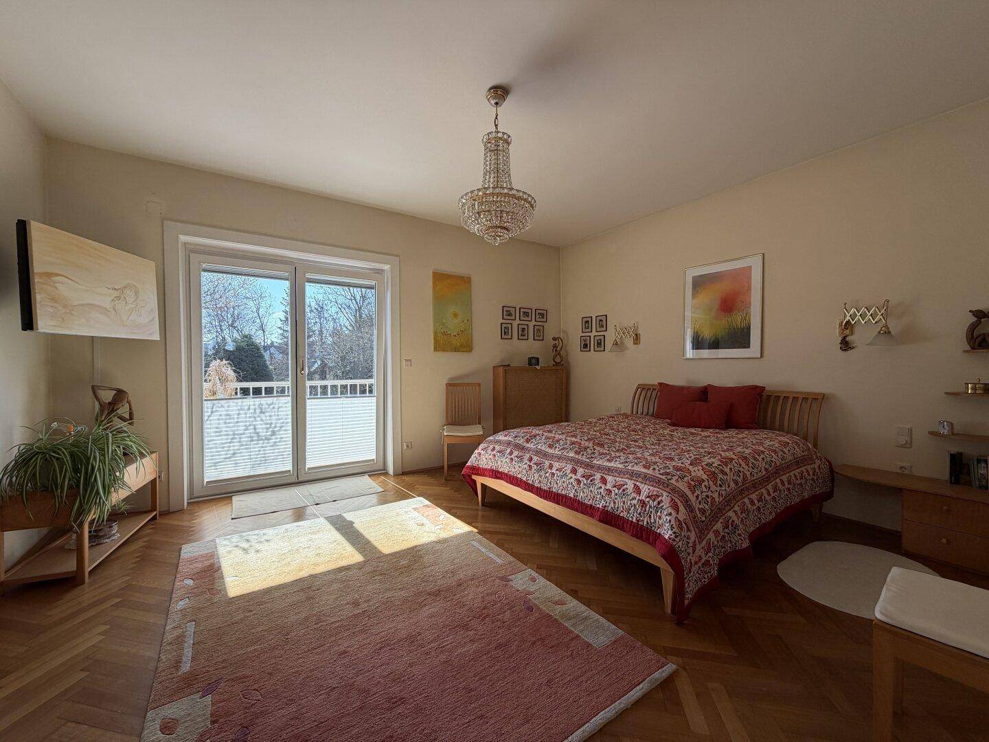 Helles Schlafzimmer mit Doppelbett, Kronleuchter und direktem Zugang zu einem sonnigen Balkon.