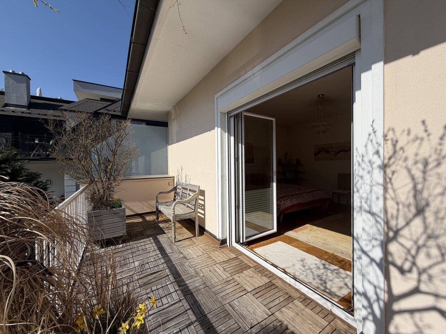 Sonniger Balkon mit Holzbelag, Sitzbank und Pflanzen, direkt vom Schlafzimmer zugänglich.