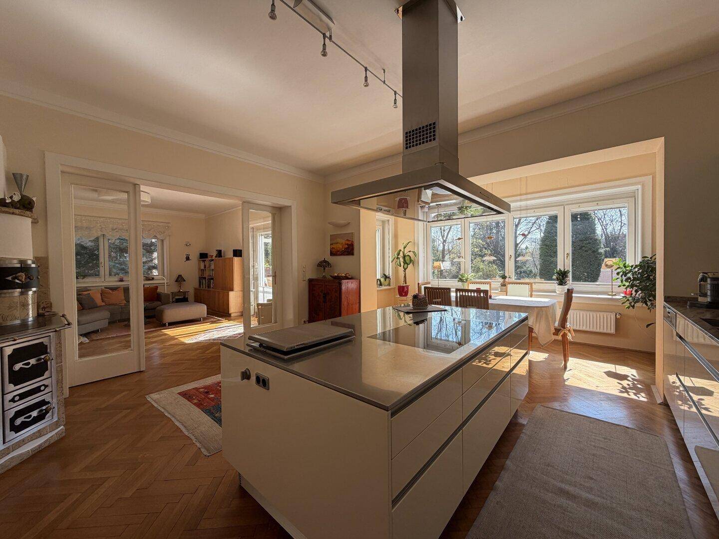 Moderne Küche mit Kochinsel und Essbereich, verbunden mit dem Wohnzimmer und Blick ins Grüne.