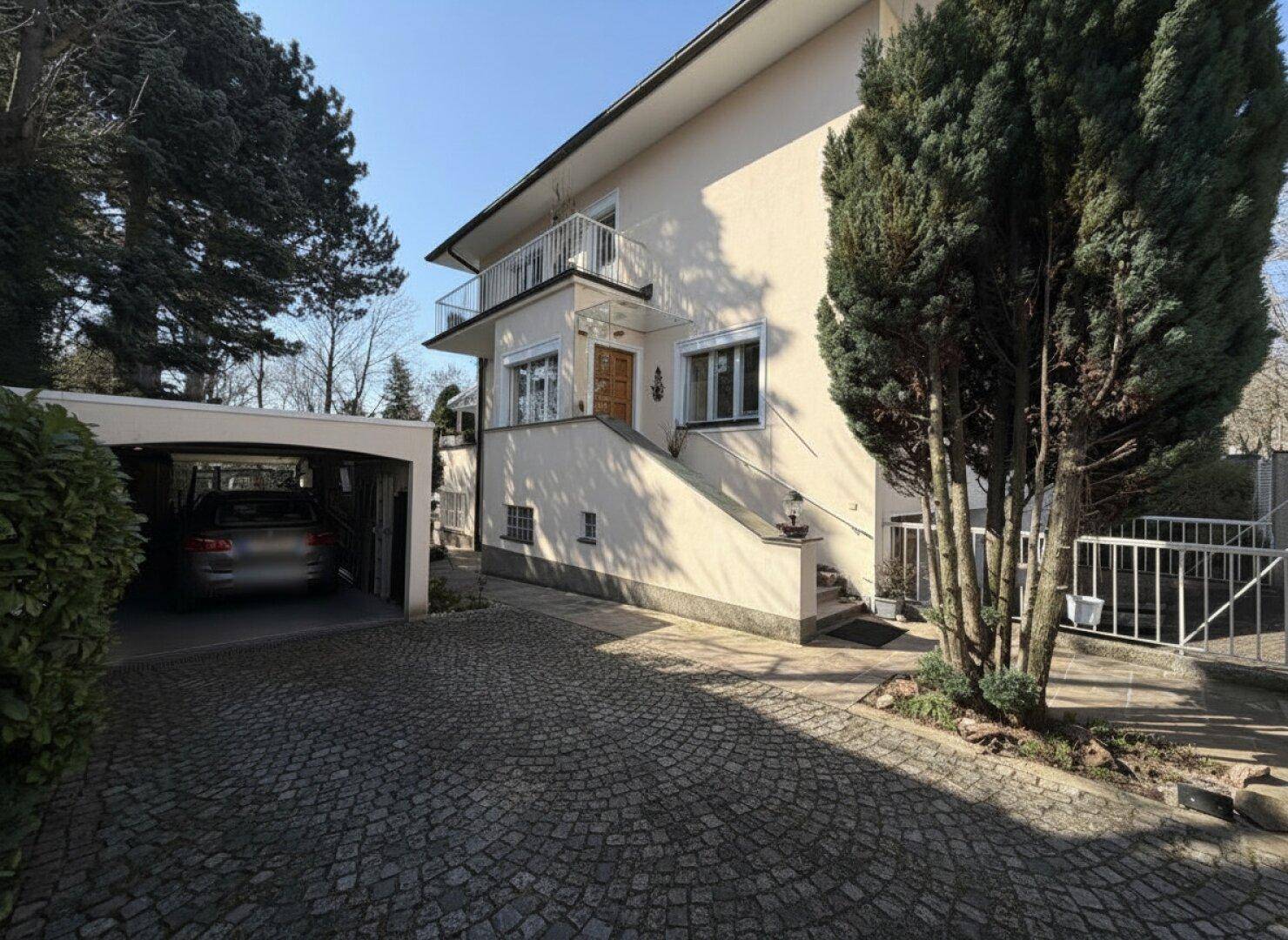 Seitenansicht des Hauses mit gepflasterter Auffahrt, Carport und Außentreppe zum Eingang.