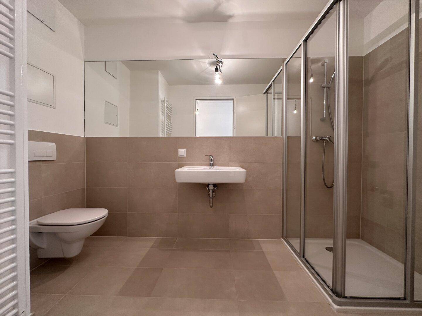 Modernes Badezimmer mit beigefarbenen Fliesen, Dusche, WC und großem Wandspiegel.