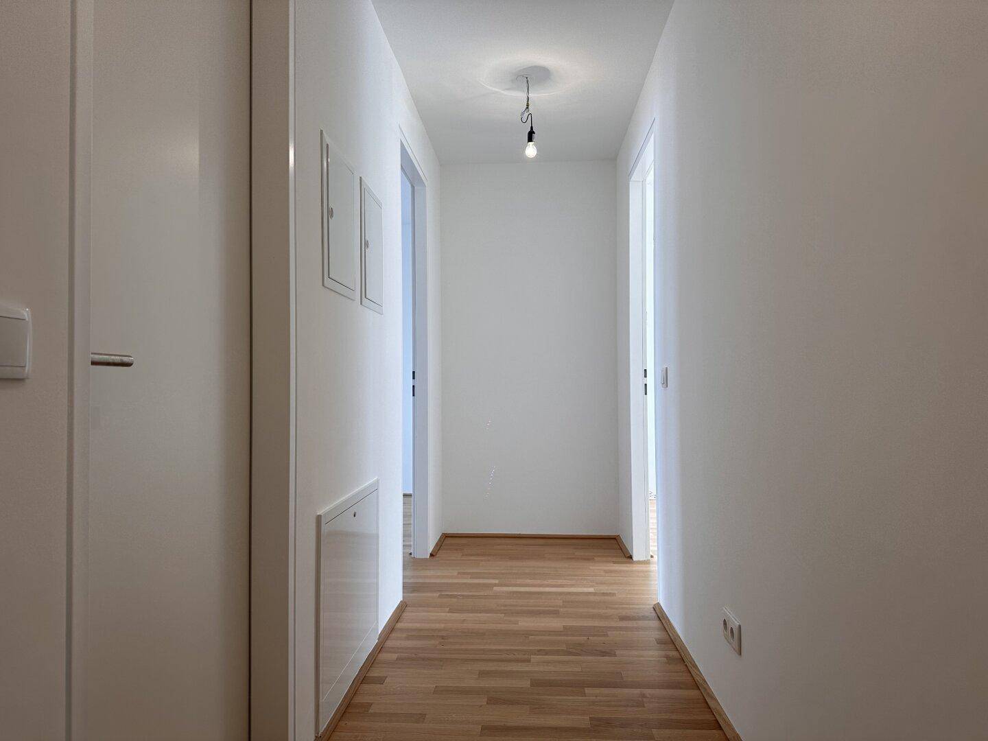 Langer, heller Flur mit Parkettboden und weißen Wänden, der verschiedene Zimmer verbindet.