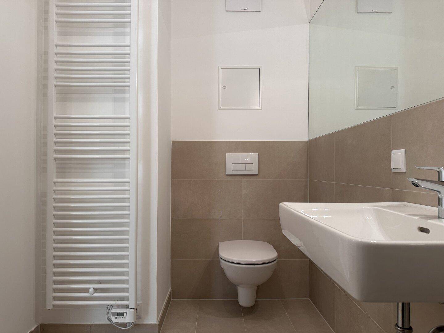 Detailansicht eines modernen Badezimmers mit WC, Waschbecken und beheiztem Handtuchhalter.