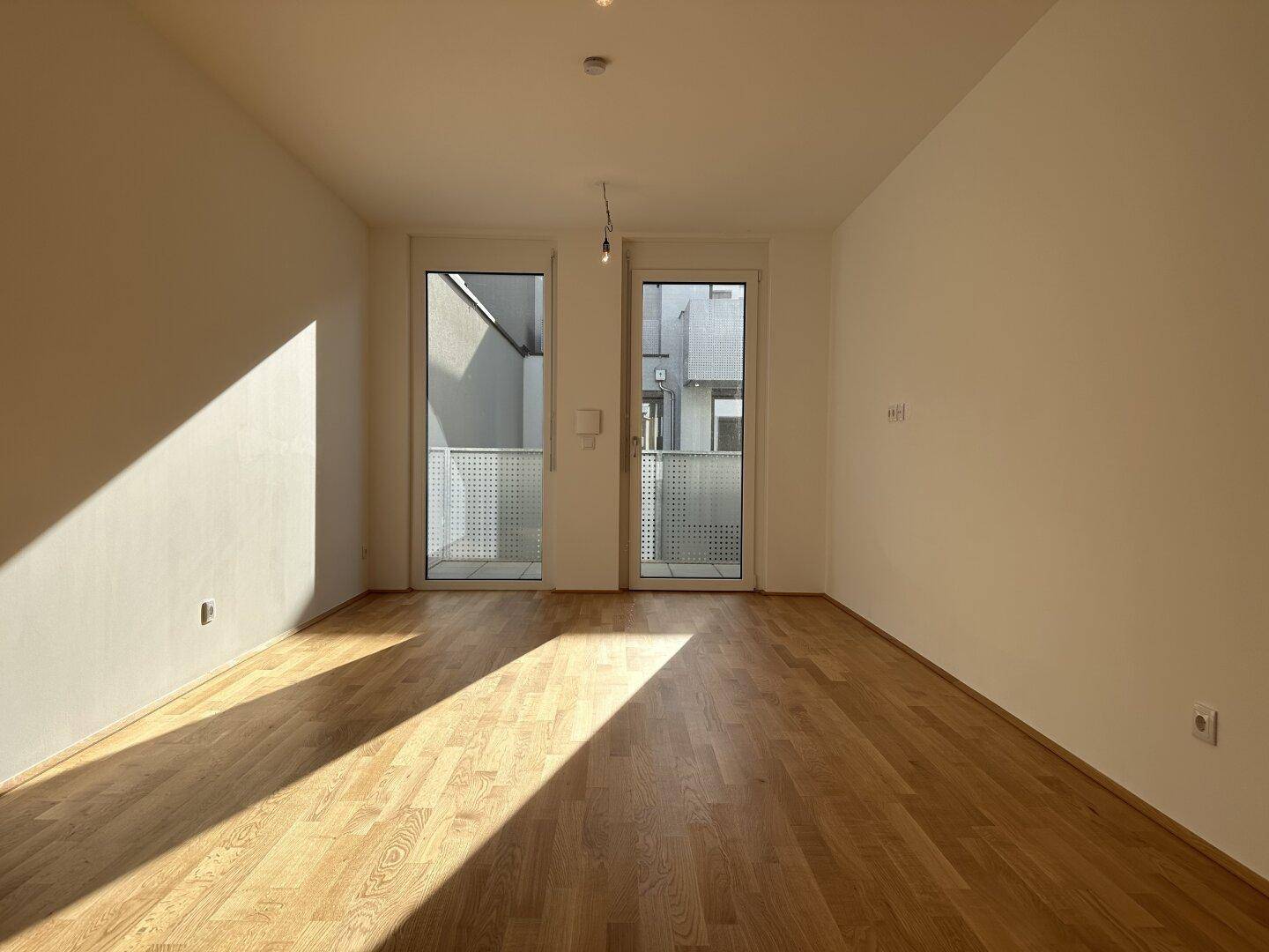 Helles Zimmer mit Parkettboden und Zugang zu einem Balkon, durchflutet von Sonnenlicht.
