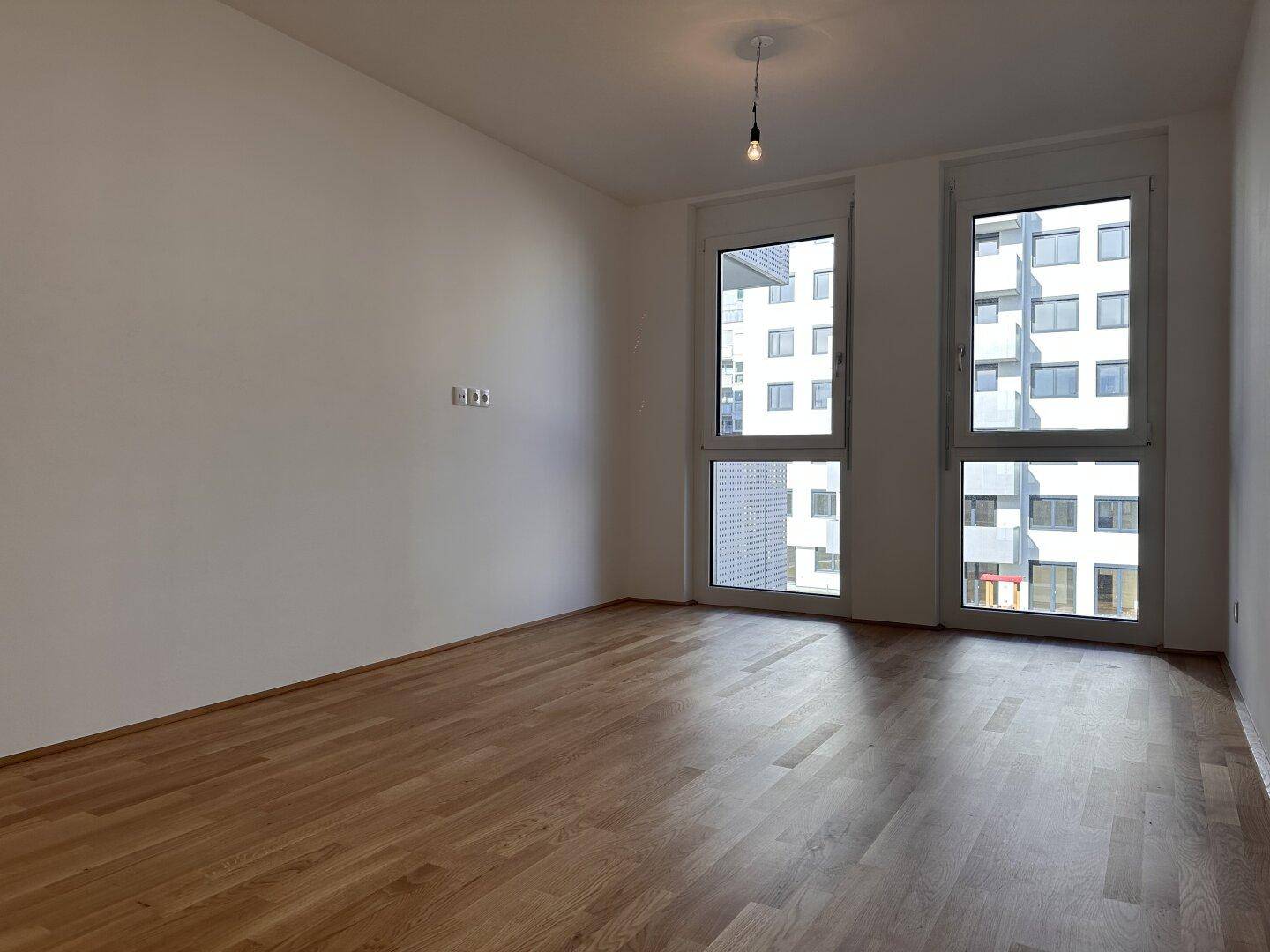 Geräumiges Zimmer mit Holzboden und großen Fenstern, die viel Tageslicht hereinlassen.