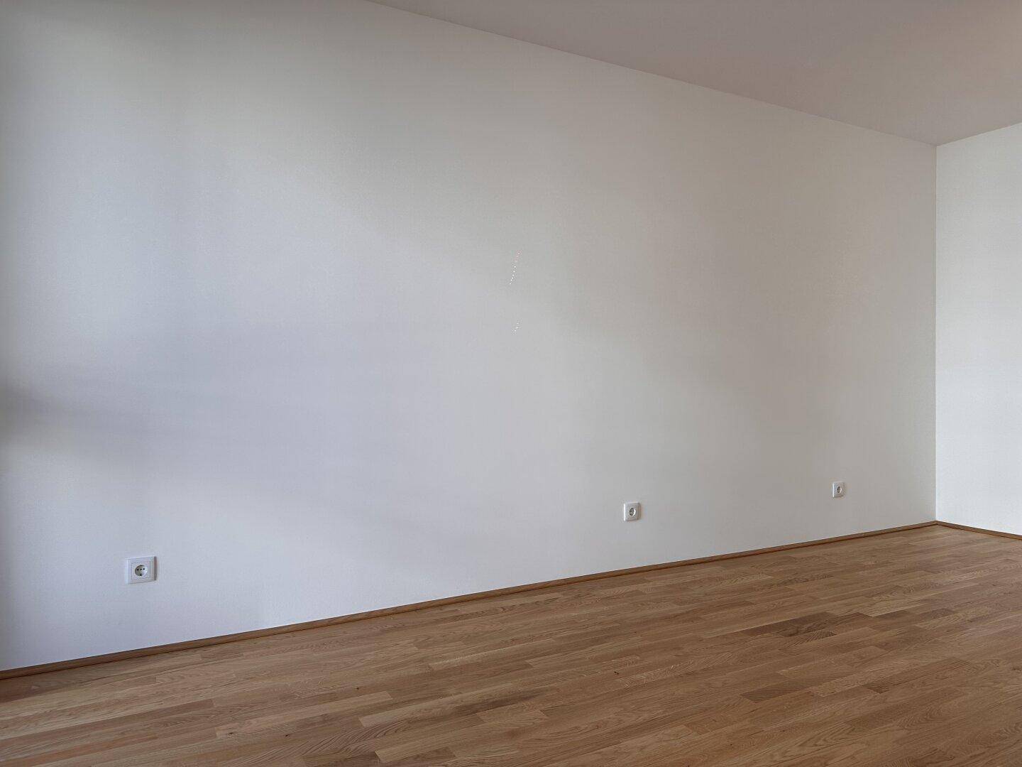 Helle Wandfläche in einem Zimmer mit Parkettboden, bereit für persönliche Dekoration.