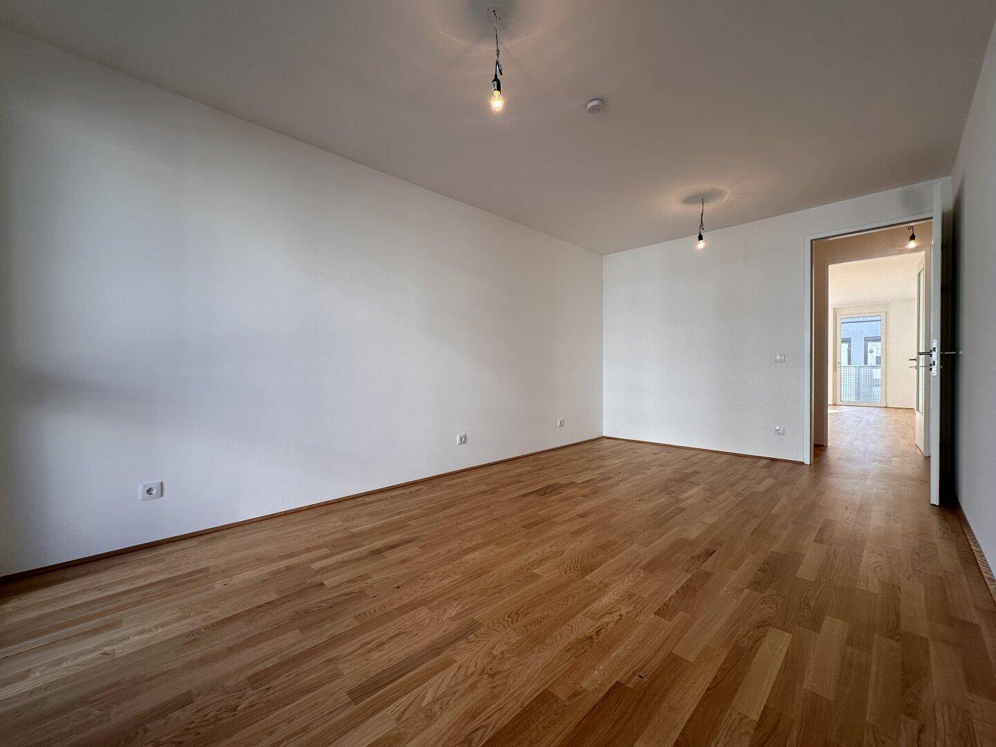 Großes, helles Zimmer mit Parkettboden und weiß gestrichenen Wänden, bietet viel Raum.