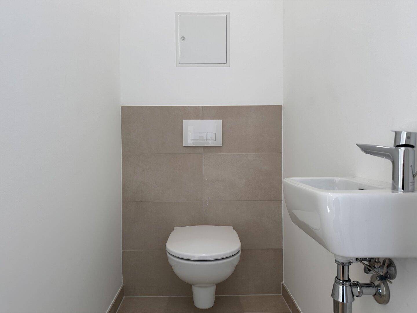 Modernes Gäste-WC mit wandhängender Toilette und kleinem Waschbecken, ausgestattet mit beigen Fliesen.