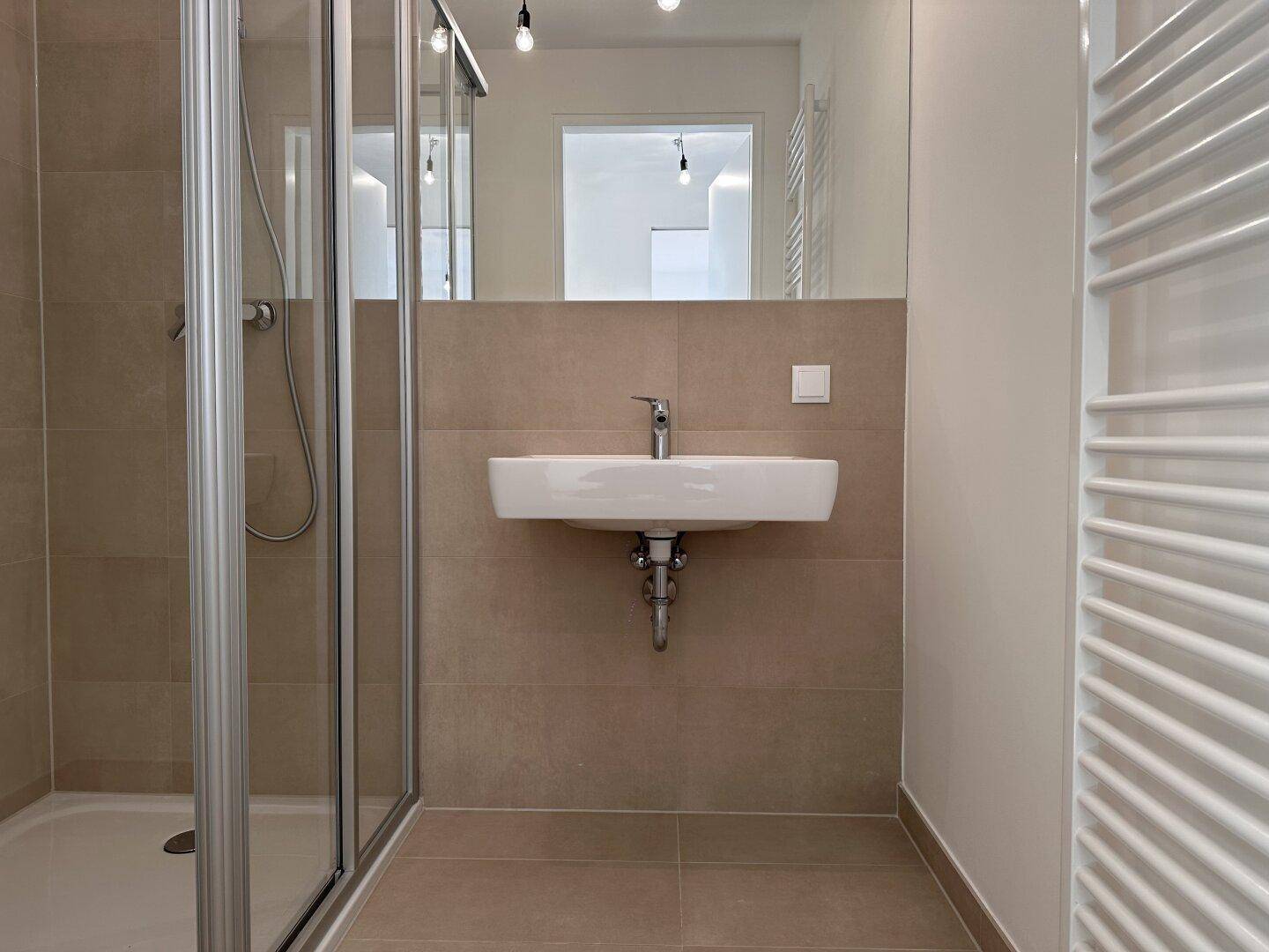 Modernes Badezimmer mit Duschkabine, Waschbecken, großem Spiegel und beheiztem Handtuchhalter.