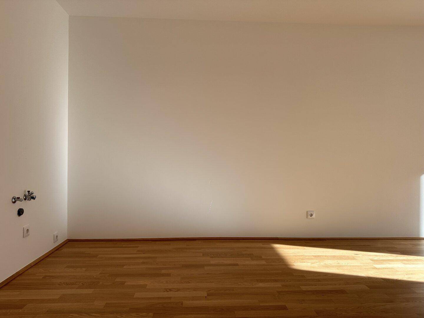 Leerer Küchenbereich mit Parkettboden und Anschlüssen für eine Einbauküche, bereit zur individuellen Gestaltung.