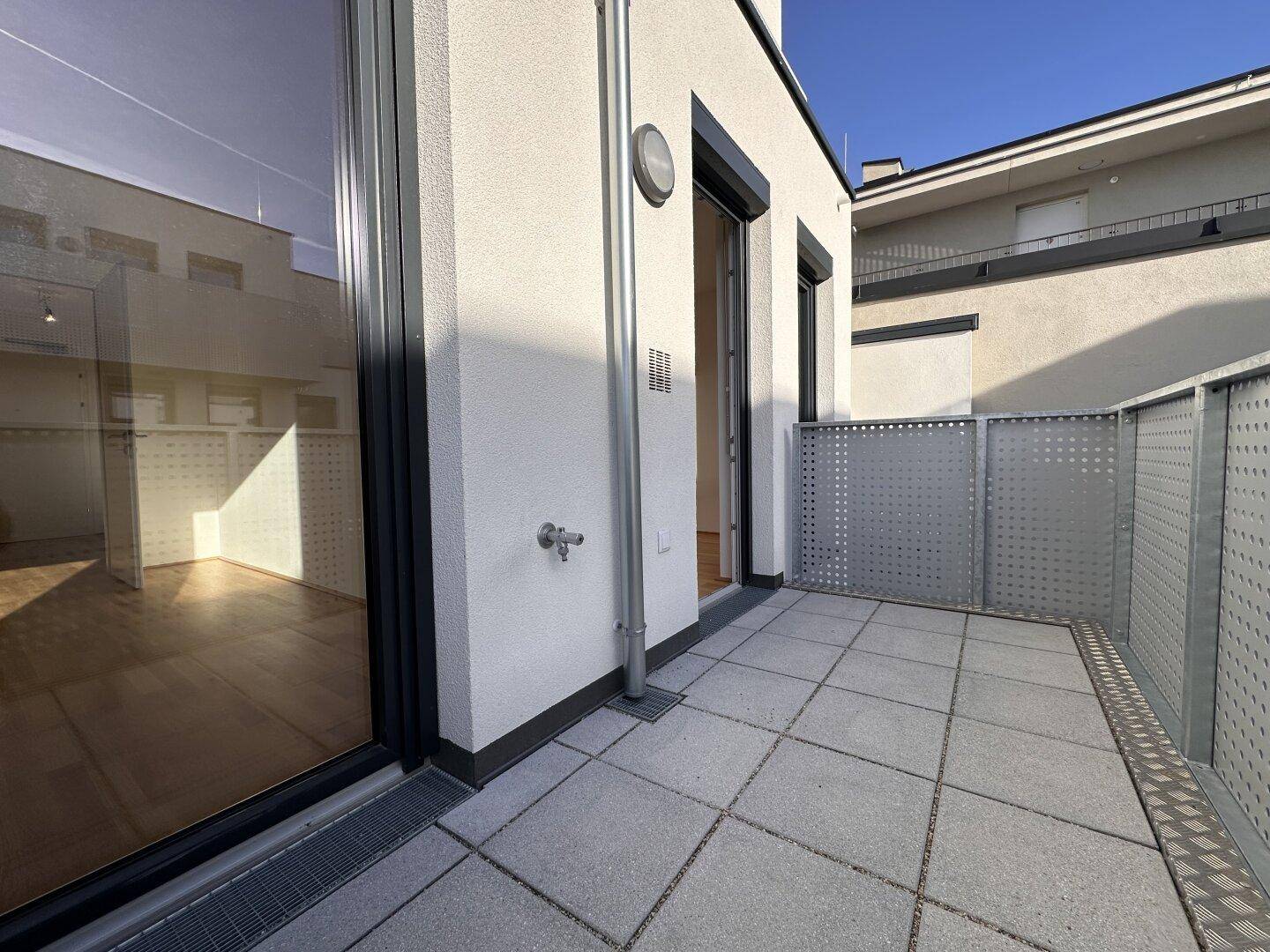 Moderner Balkon mit Fliesenboden und Metallgeländer, bietet einen privaten Außenbereich mit Zugang zum Innenraum.