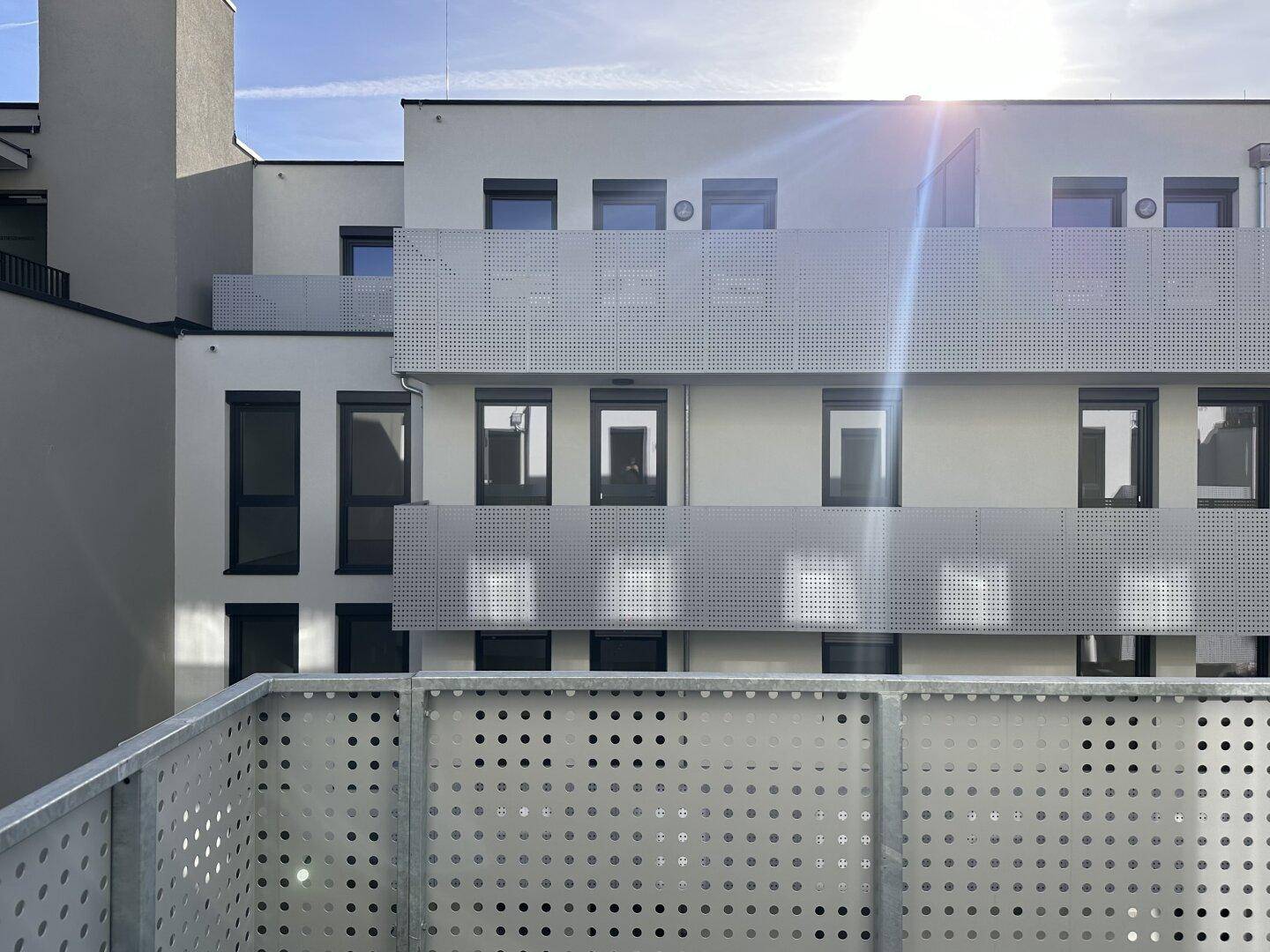Moderne Gebäudefassade mit mehreren Balkonen und perforierten Metallgeländern unter strahlendem Sonnenschein.