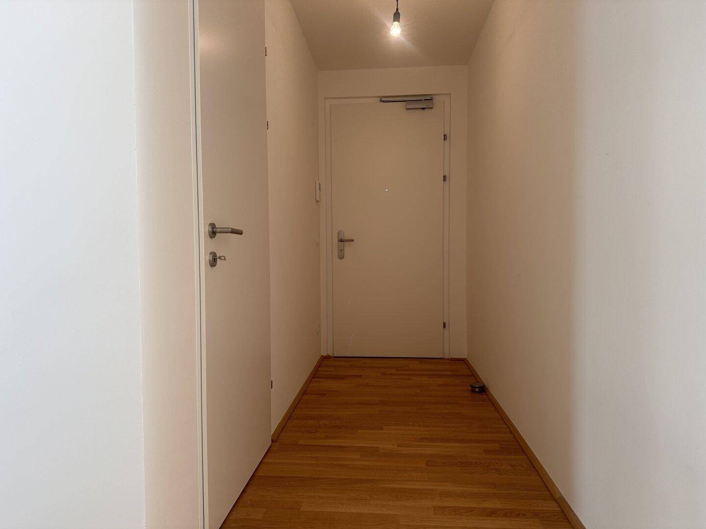 Heller Flur mit Holzboden und weißer Eingangstür, der zu den Wohnräumen führt.