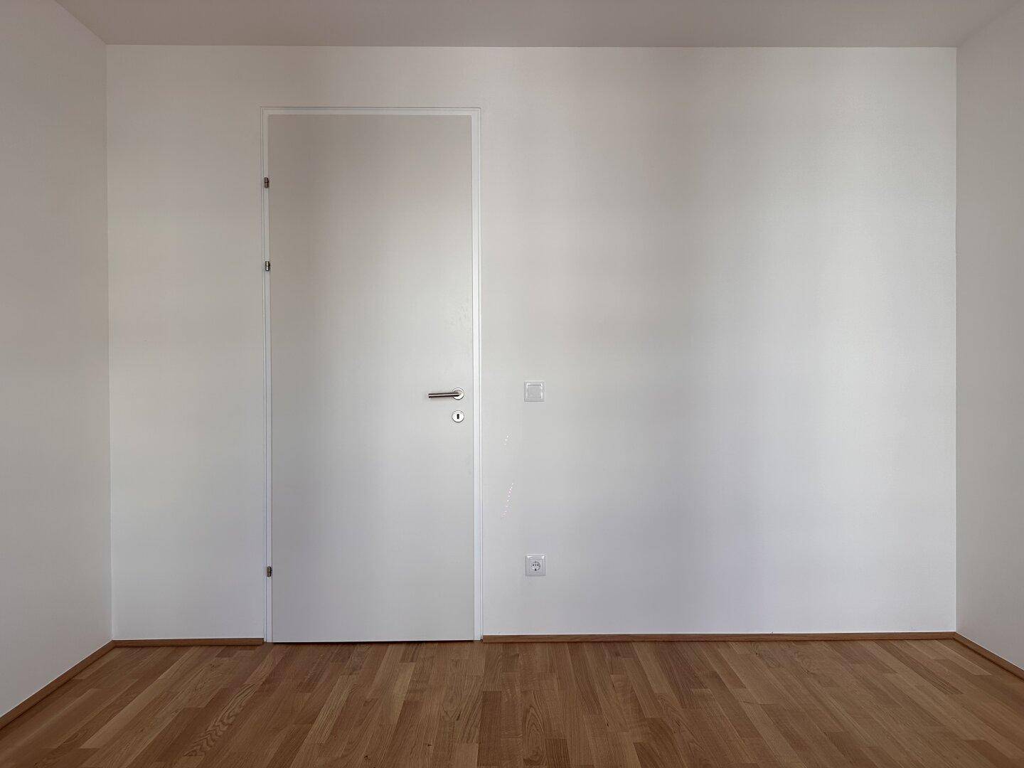 Leerer Raum mit Parkettboden und einer weißen Tür, bereit zur individuellen Gestaltung.