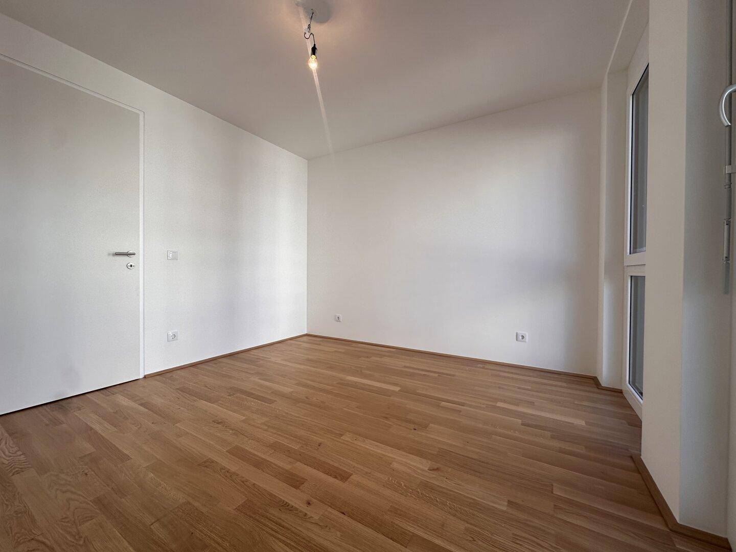 Geräumiges, helles Zimmer mit Parkettboden und viel Tageslicht durch die Fenster.