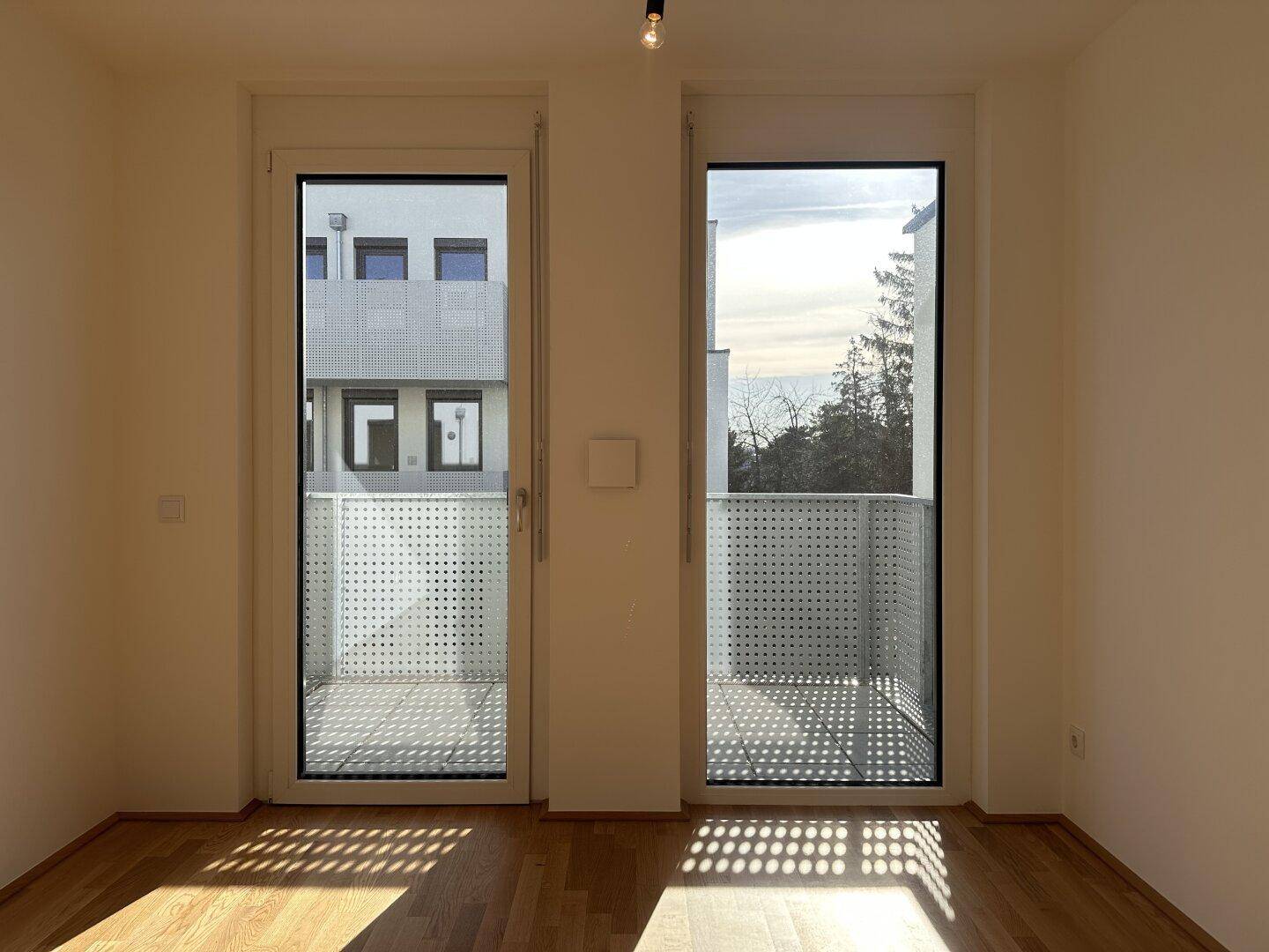 Heller Wohnbereich mit Parkettboden und Zugang zu einem französischen Balkon.