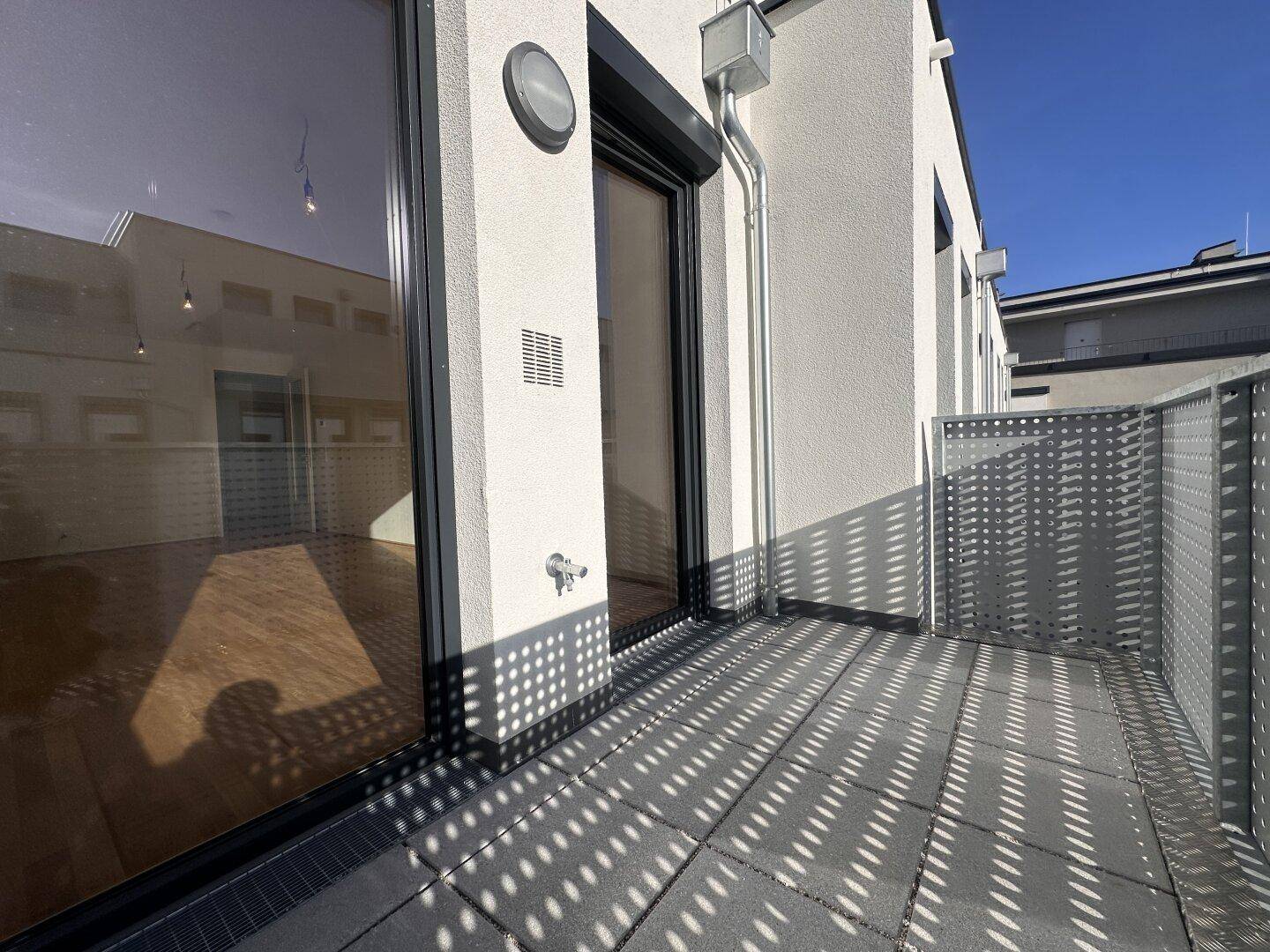 Moderner Balkon mit Fliesenboden und perforiertem Geländer, sonnig und hell.