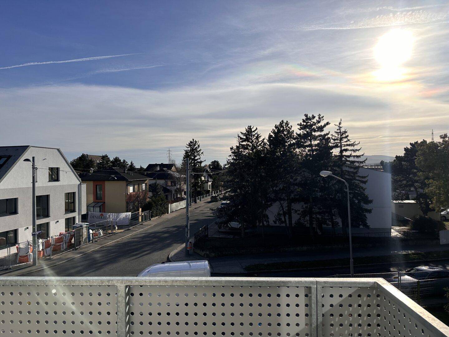 Sonniger Ausblick von einem Balkon auf die umliegende Wohngegend und Bäume.