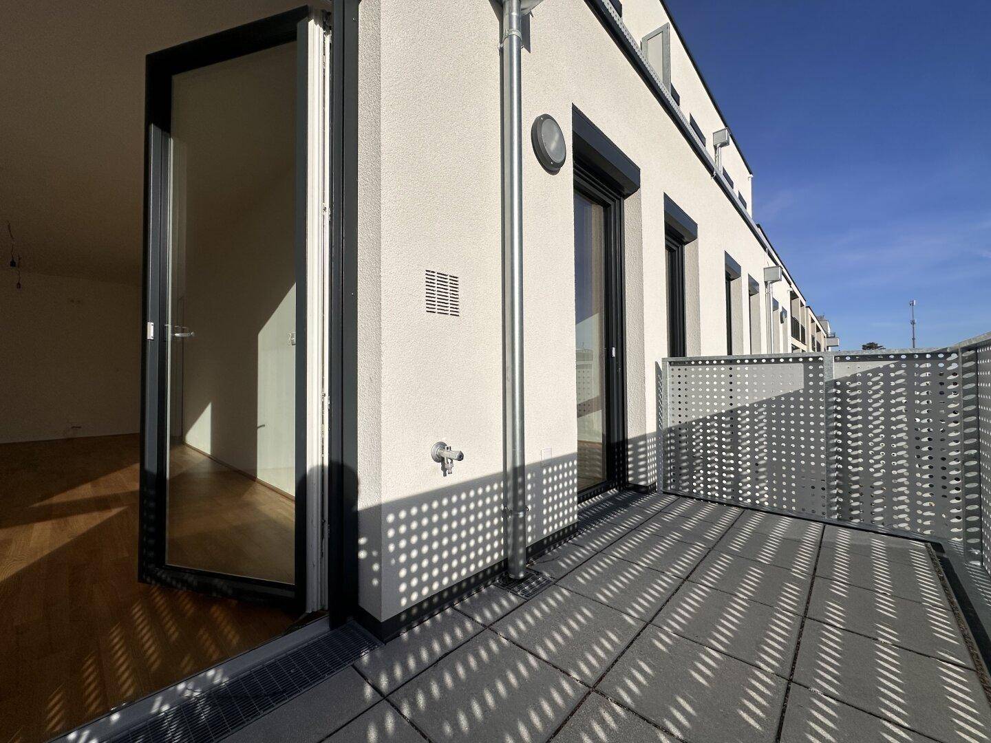 Moderner Balkon mit perforiertem Geländer und Zugang zu einem hellen Innenraum.