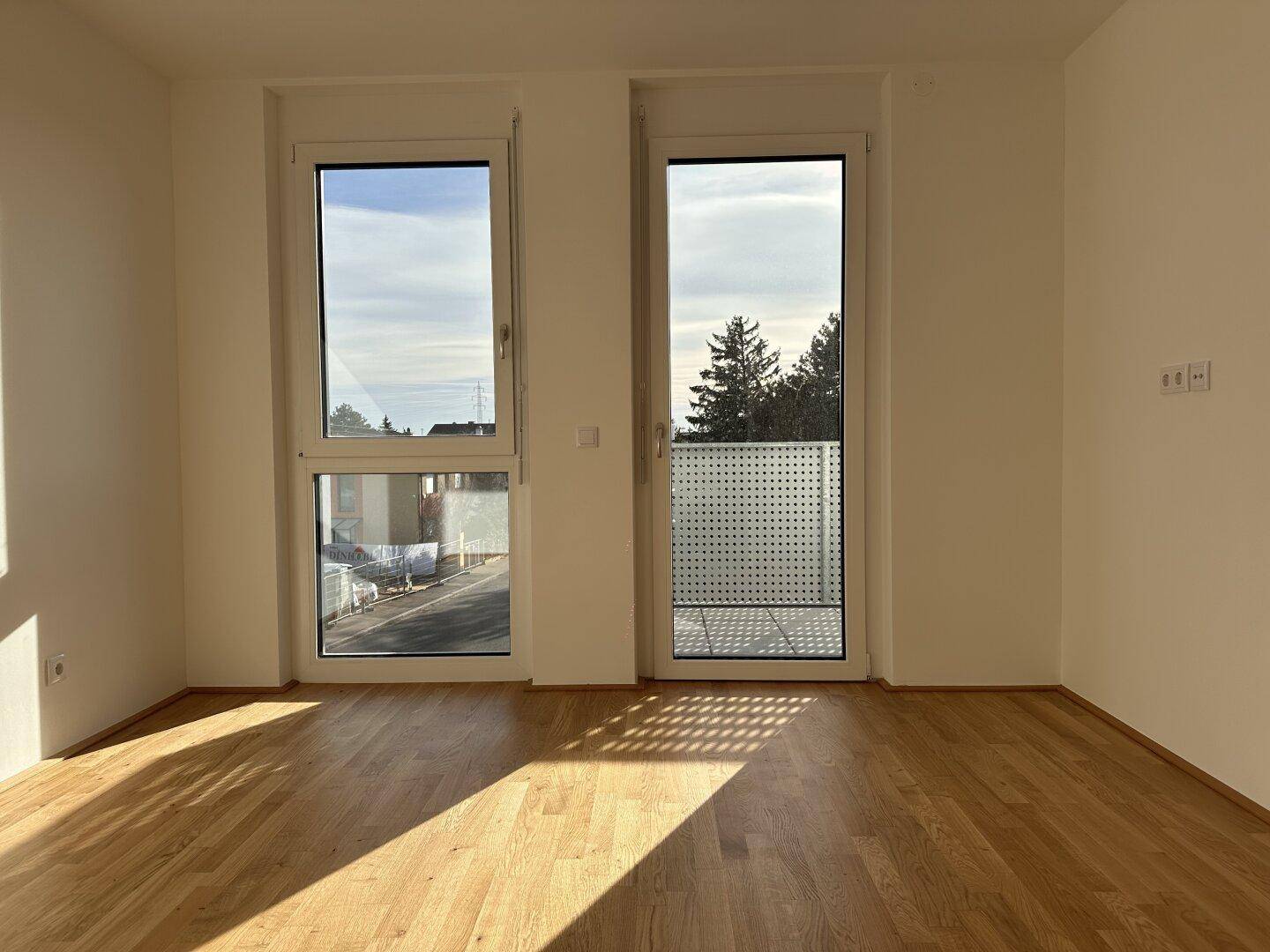 Heller Raum mit Holzboden und großen Fenstern, die viel Licht hereinlassen.