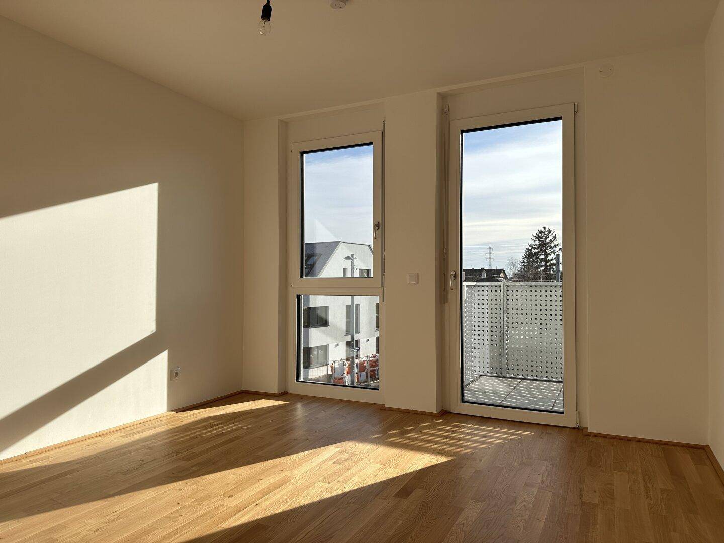 Lichtdurchfluteter Raum mit Holzboden und Blick auf die umliegenden Gebäude.