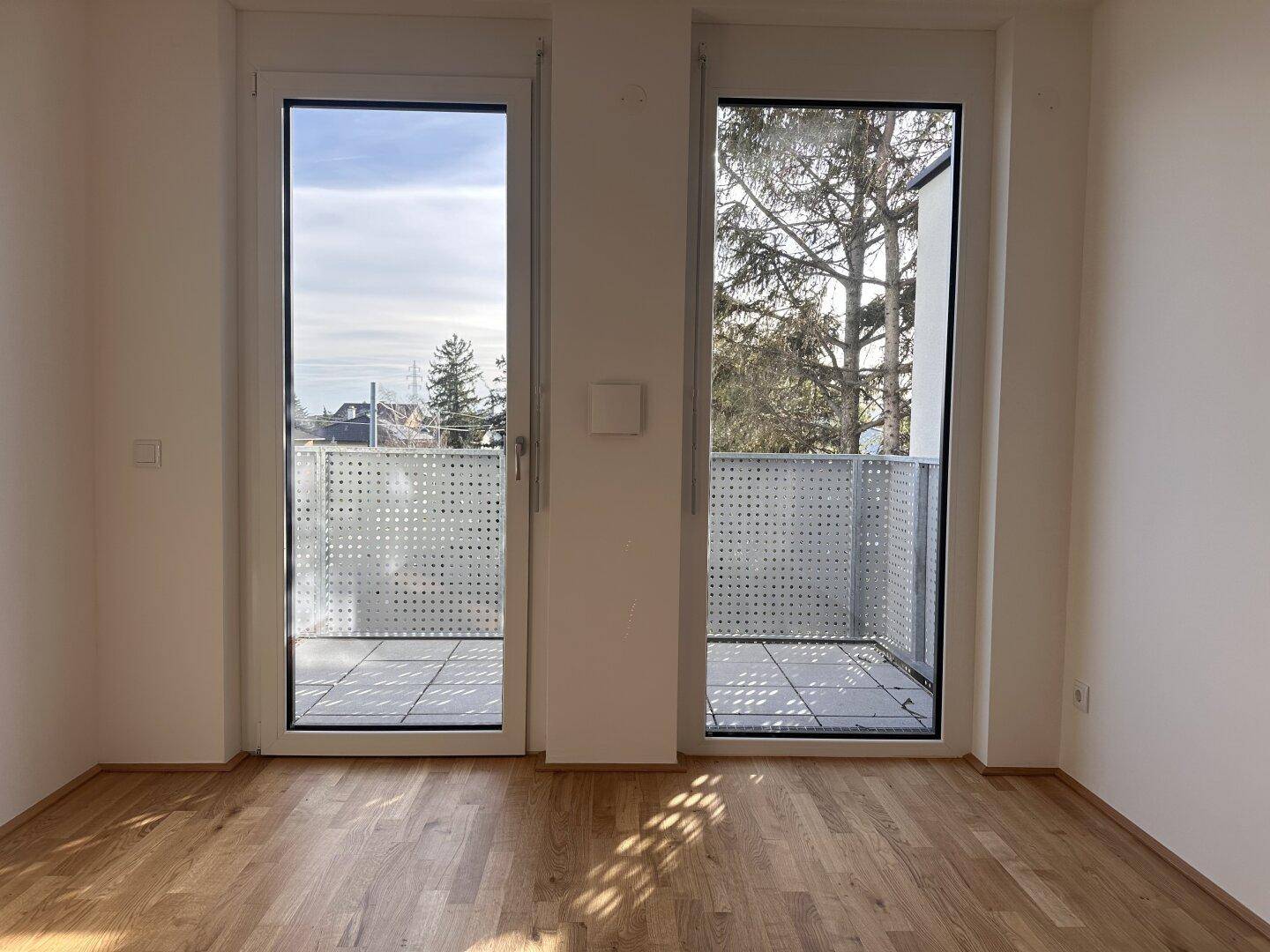 Lichtdurchfluteter Raum mit Holzboden und Blick auf die Umgebung durch die Balkontür.