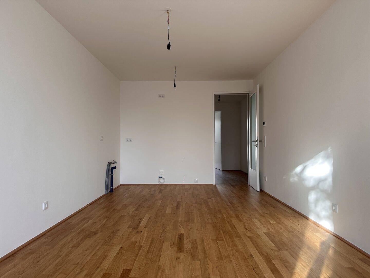 Geräumiger, leerer Raum mit Holzboden und weiß gestrichenen Wänden, bereit zur Einrichtung.