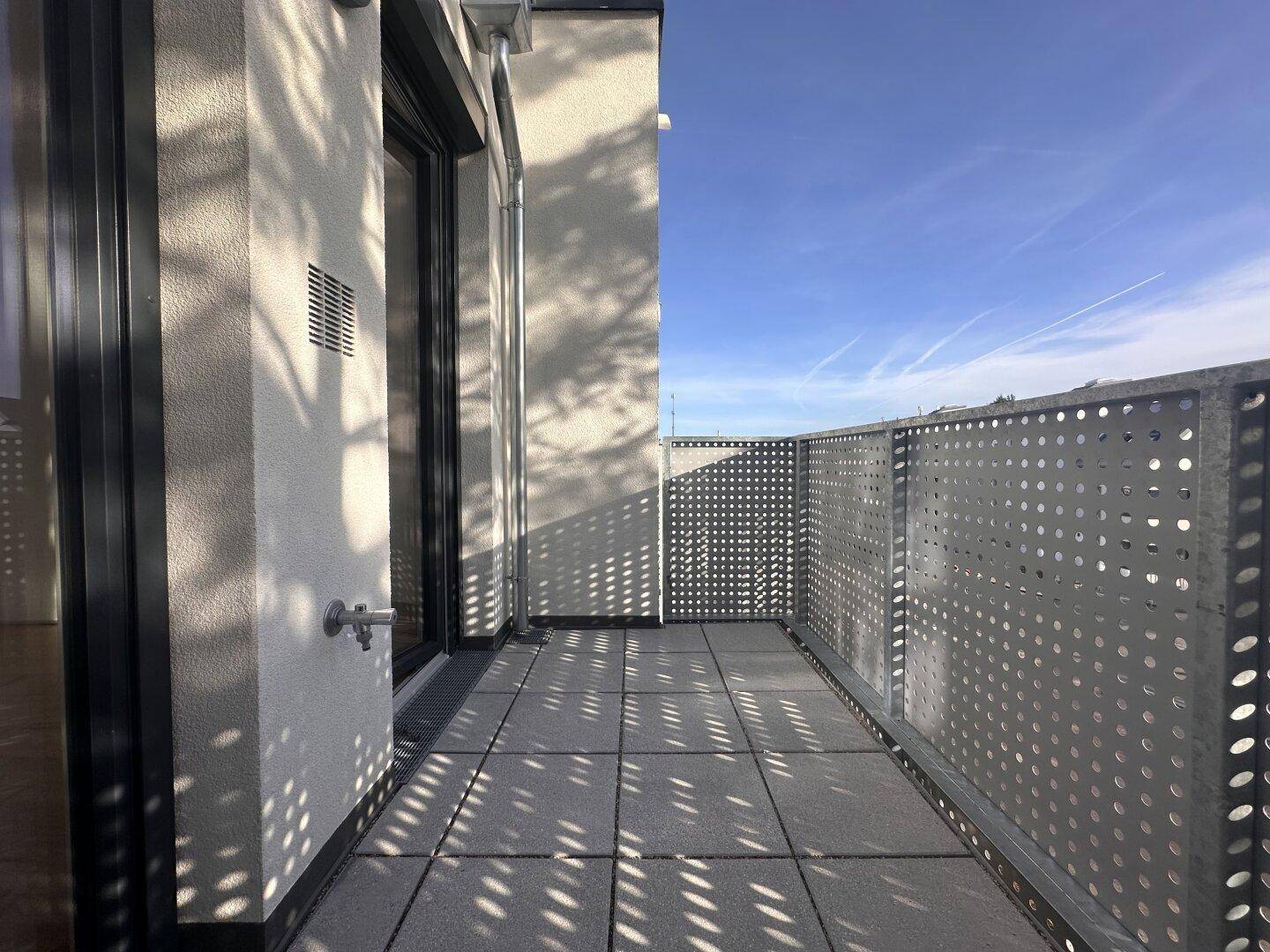 Moderner Balkon mit Fliesenboden und perforiertem Metallgeländer, sonnig und hell.