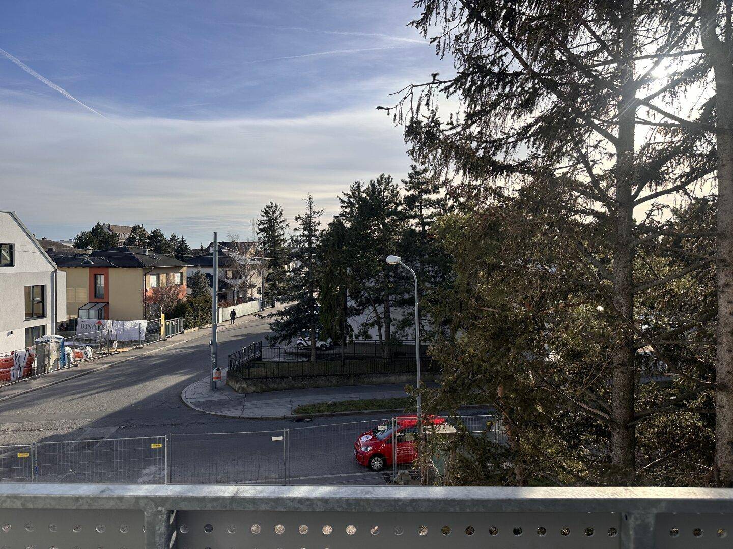 Ausblick vom Balkon auf die Wohngegend mit Bäumen und einer Straße, bei sonnigem Wetter.