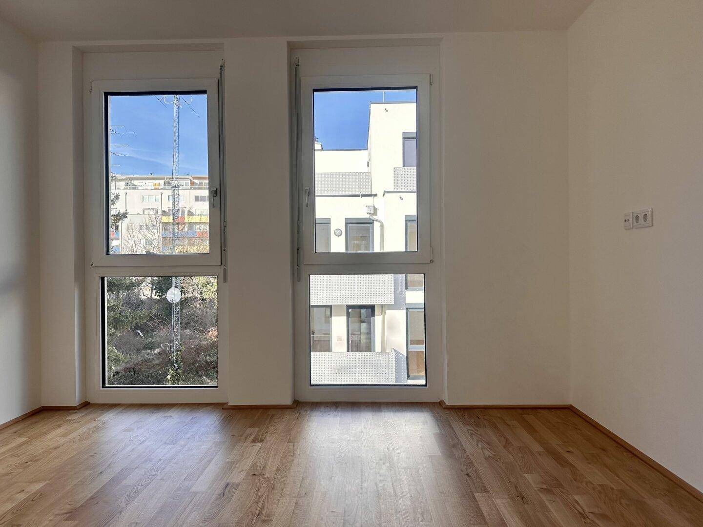 Heller Raum mit Holzboden und großen Fenstern, die viel Tageslicht hereinlassen.