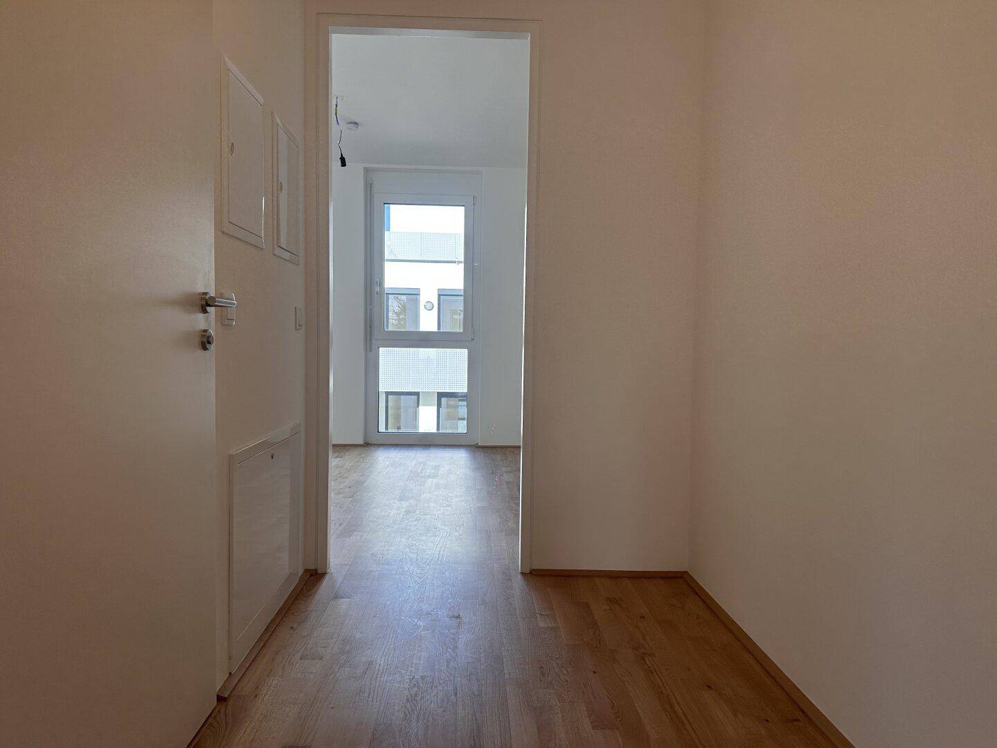 Heller Flur mit Holzboden, der zu einem weiteren Zimmer mit Fenstern führt.