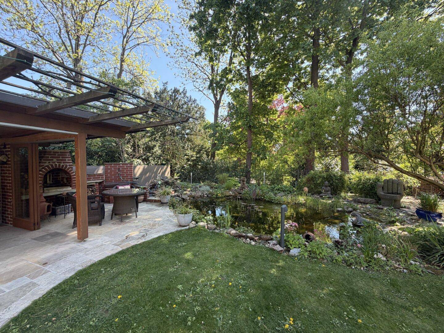 Weitläufiger Garten mit Terrasse, Teich und altem Baumbestand, ideal für Entspannung im Freien.