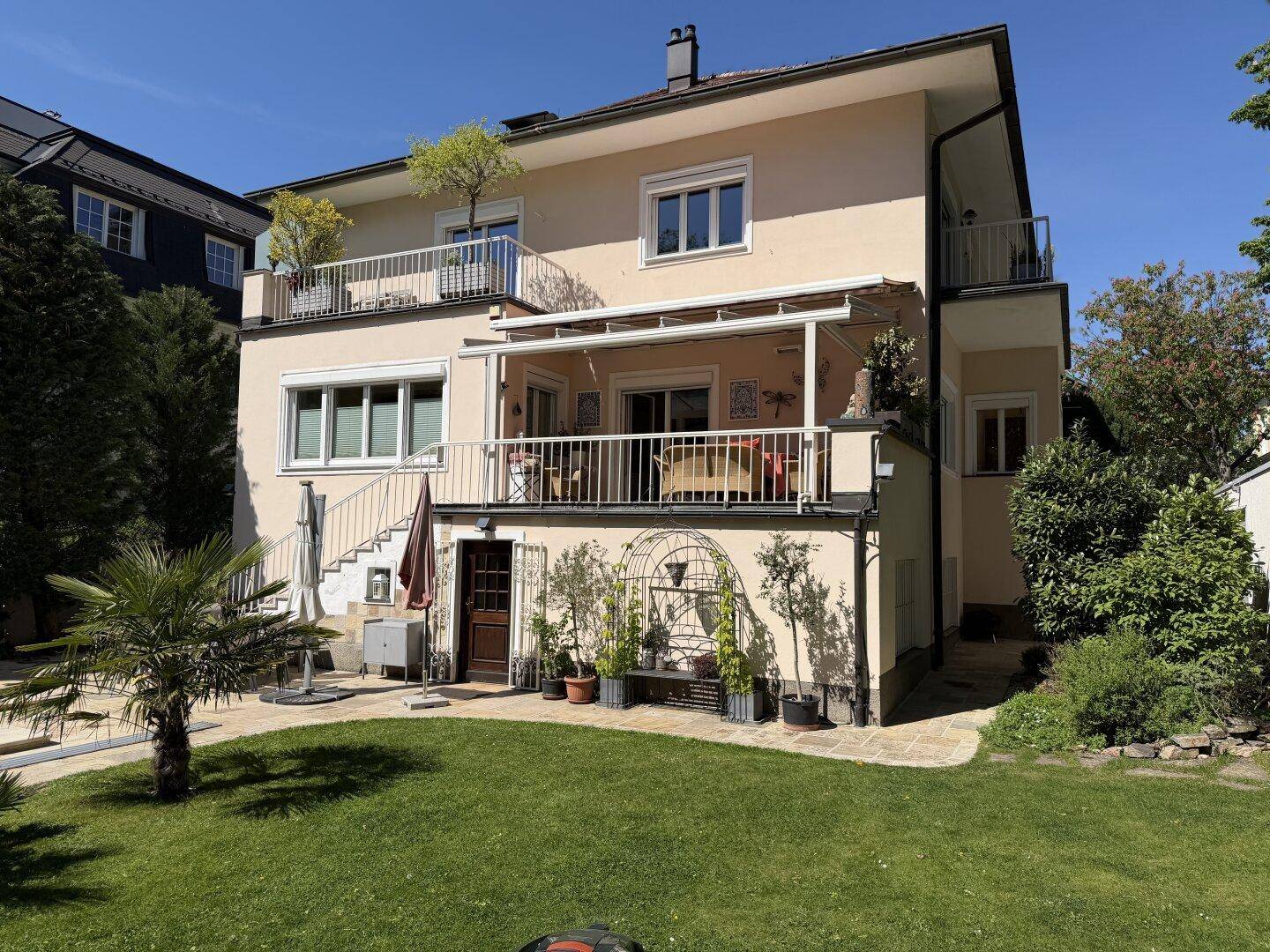 Rückansicht des Hauses mit mehreren Balkonen und einer überdachten Terrasse, umgeben von Grün.