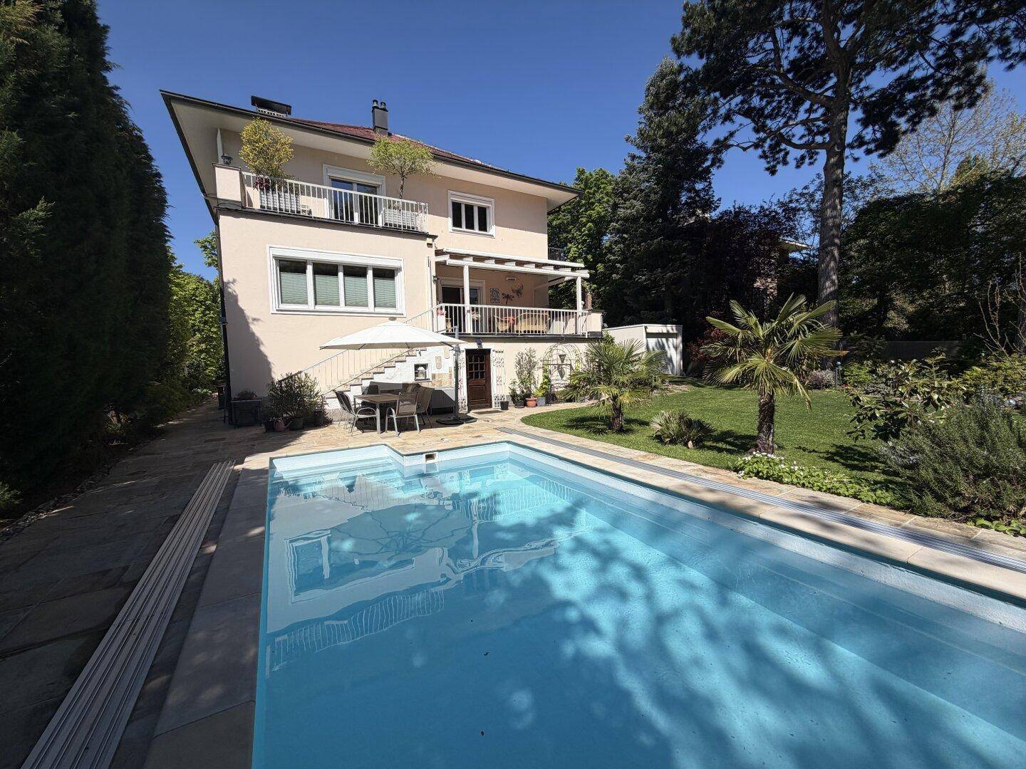 Weitläufiger Außenbereich mit großem Swimmingpool, Liegefläche und gepflegtem Garten unter blauem Himmel.