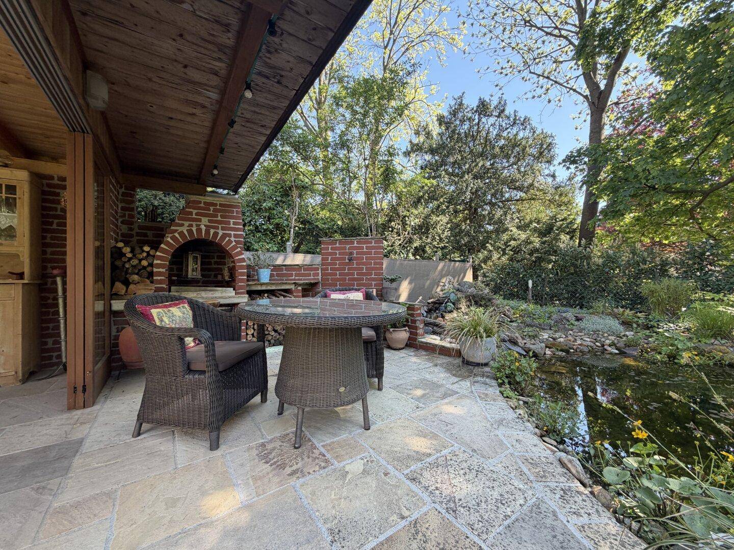 Gemütlicher Terrassenbereich mit Essgruppe, gemauertem Grill und Blick auf den Gartenteich.