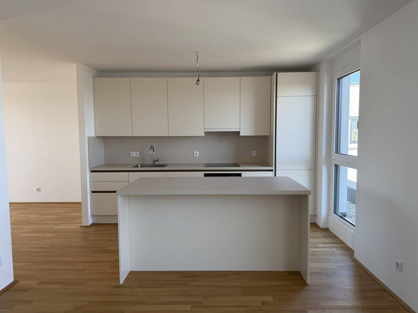 Moderne Einbauküche mit hellen Schränken, Kücheninsel und Blick auf die Stadt durch große Fenster.