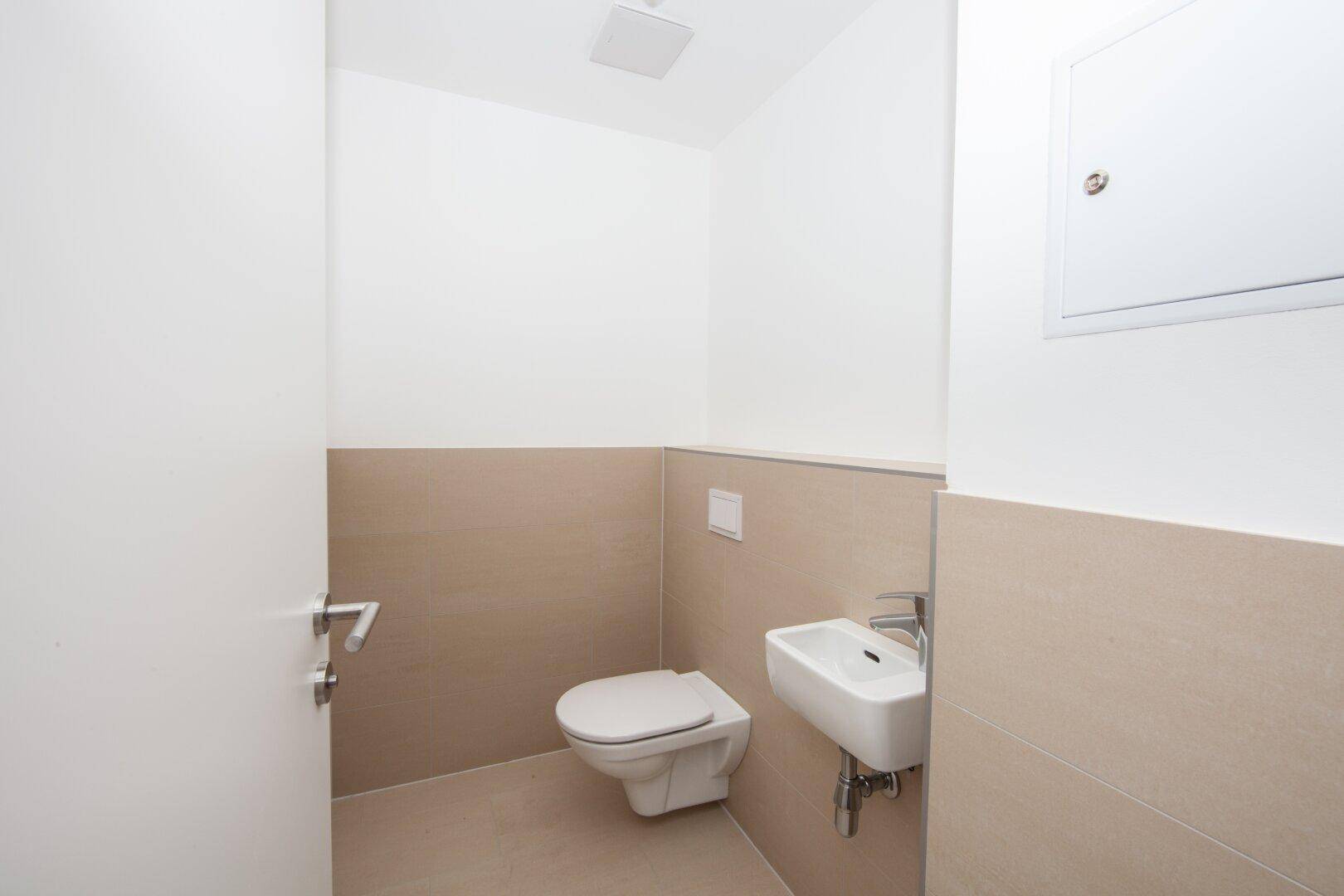 Modernes Gäste-WC mit Wand-WC, kleinem Waschbecken und beigefarbenen Fliesen.