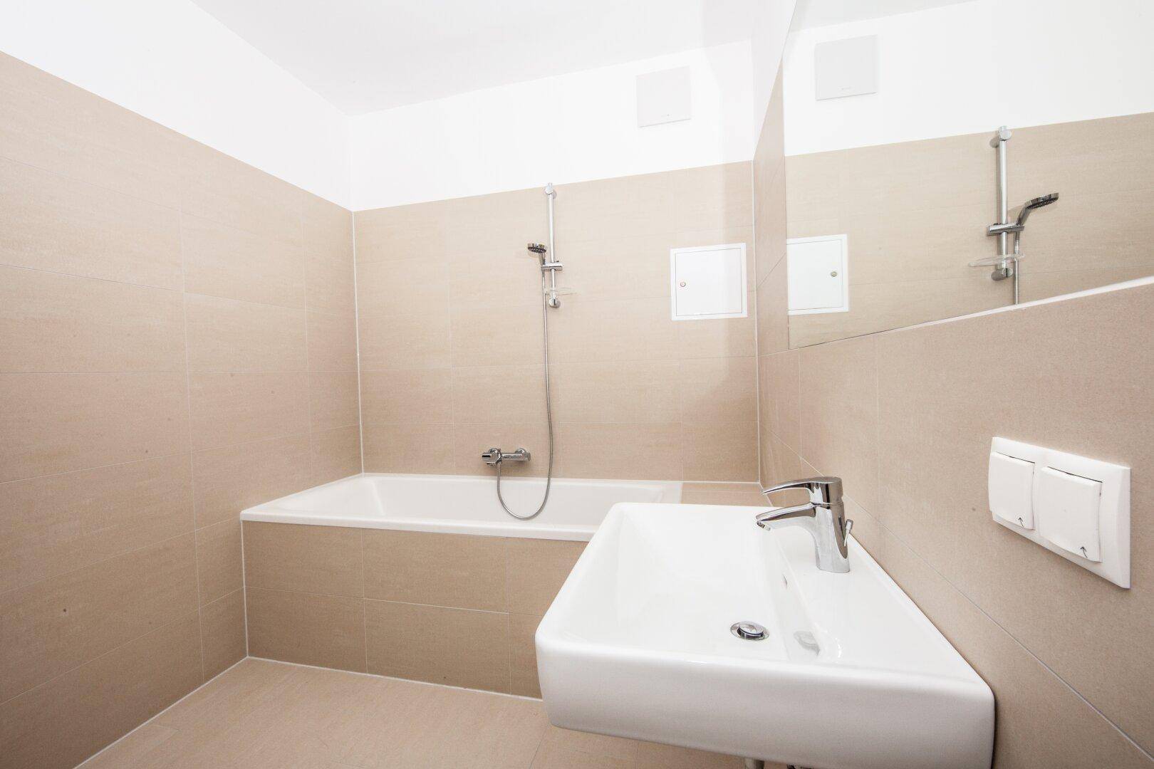 Helles Badezimmer mit Badewanne, Waschbecken und großem Spiegel, gefliest in Beige.