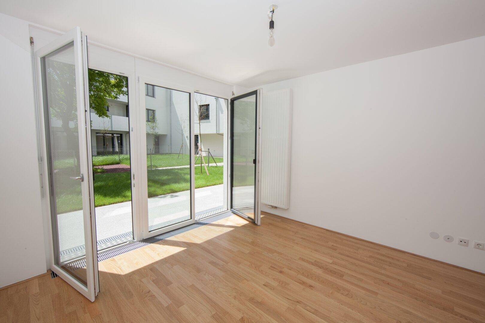 Helles Zimmer mit Parkettboden und bodentiefen Fenstern, die Zugang zum Außenbereich bieten.