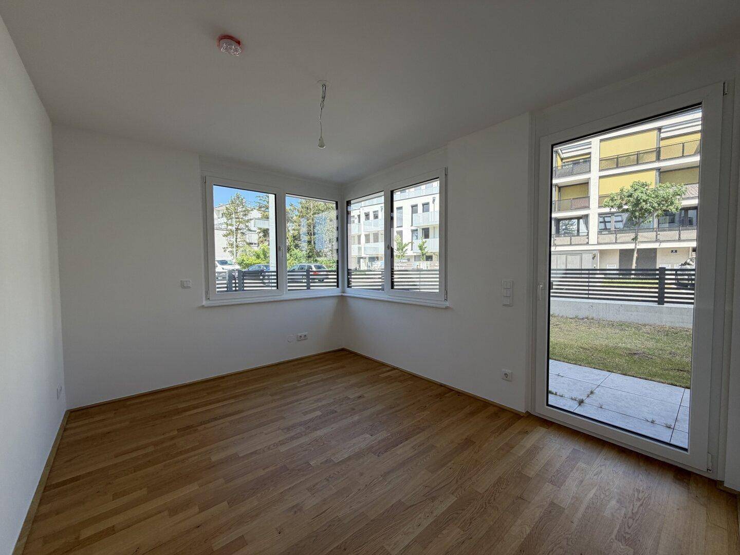 Leeres Schlafzimmer mit Holzboden, großen Fenstern und Zugang zu einem Außenbereich.