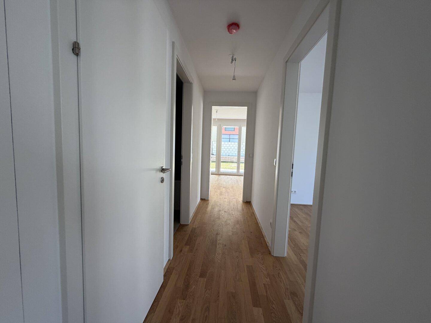 Heller Flur mit Holzboden und weißen Türen, der zu weiteren Räumen führt.