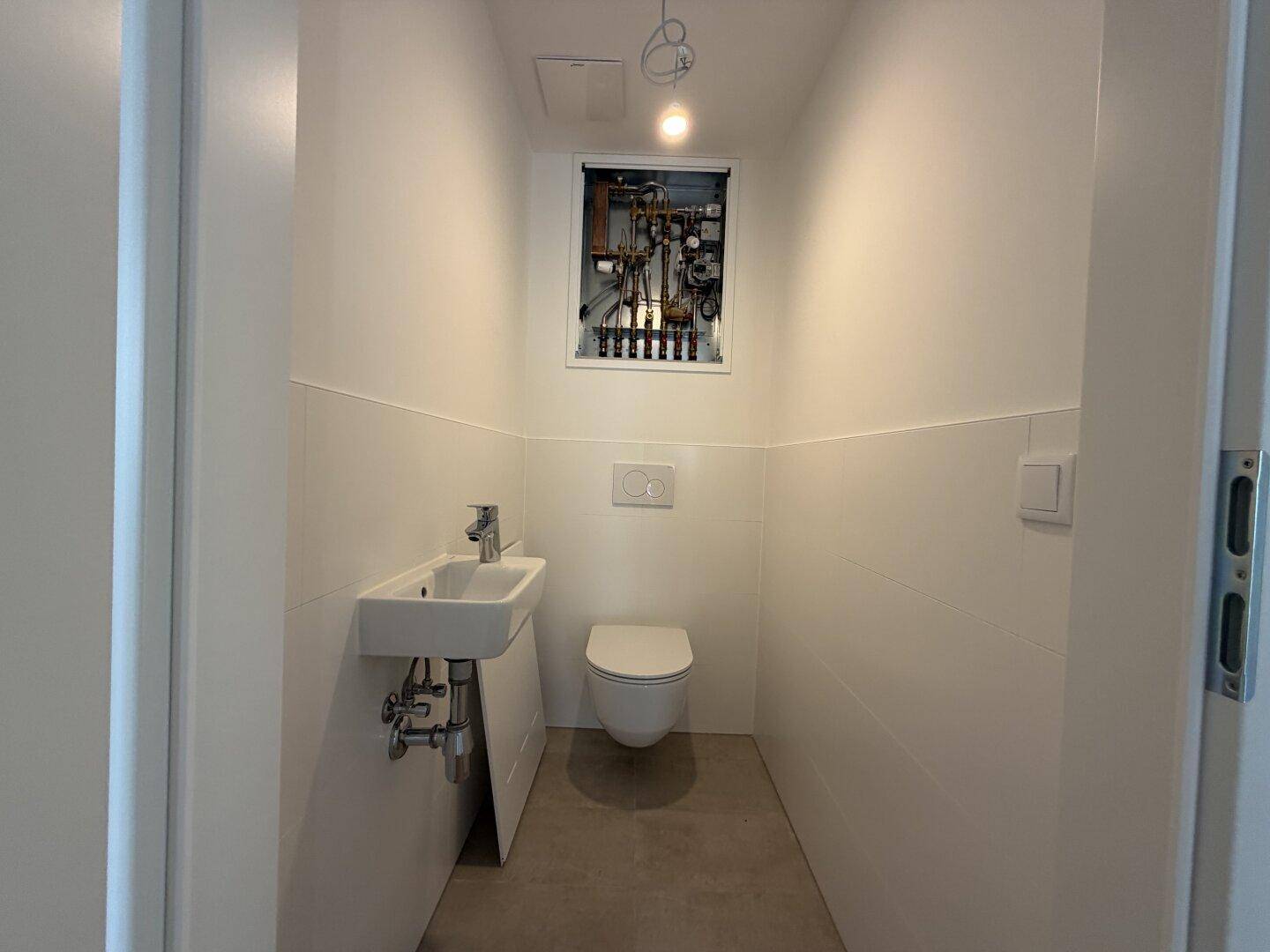 Modernes Gäste-WC mit wandhängender Toilette, kleinem Waschbecken und weißen Fliesen.