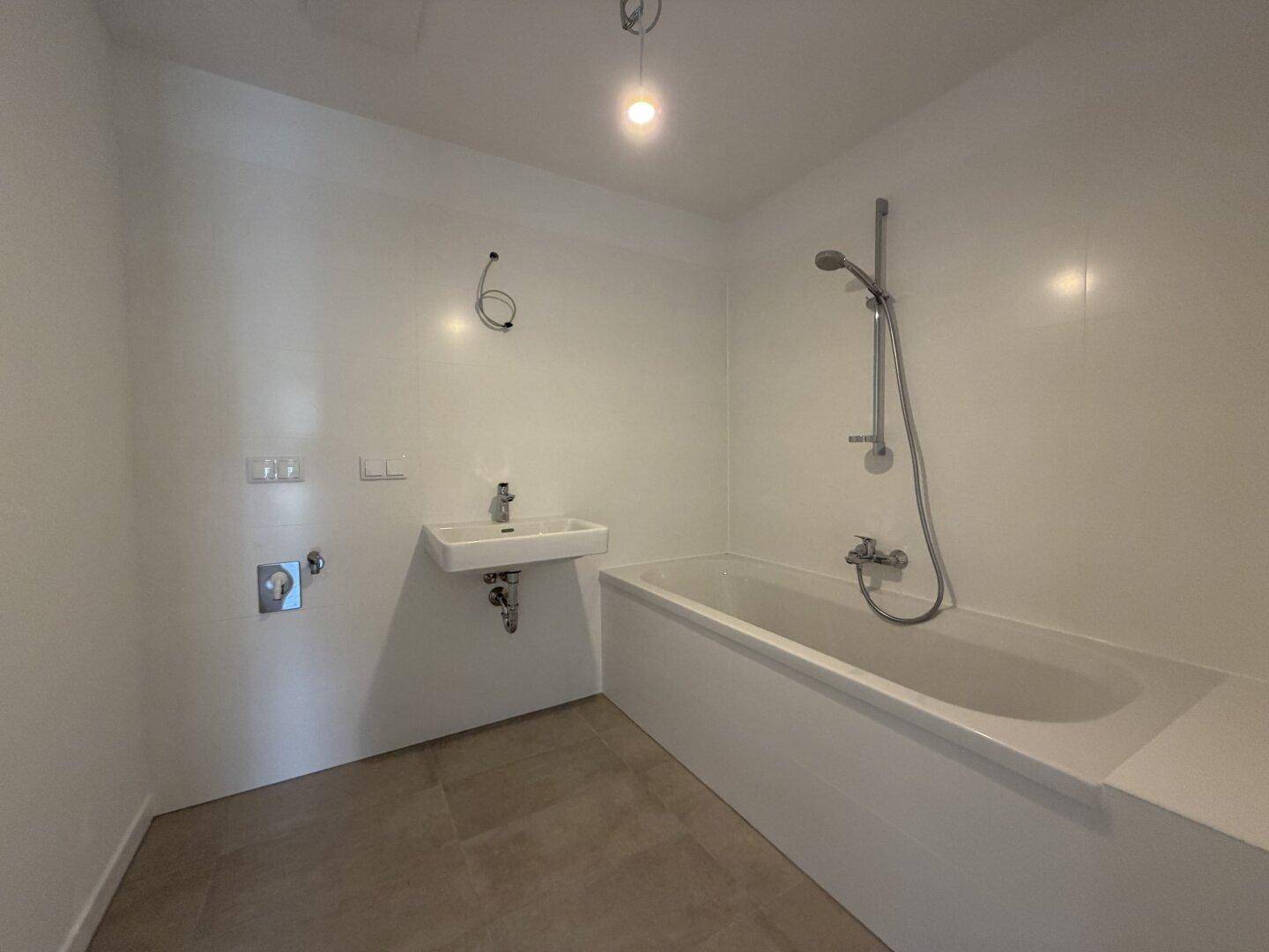 Helles Badezimmer mit Badewanne, Waschbecken und weißen Wandfliesen, bereit zur Fertigstellung.