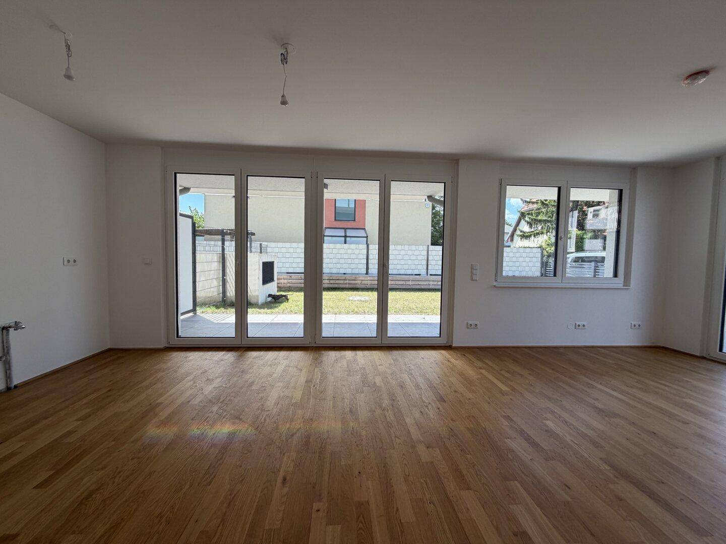 Geräumiger Wohnbereich mit Holzboden und breiter Fensterfront zum Garten.